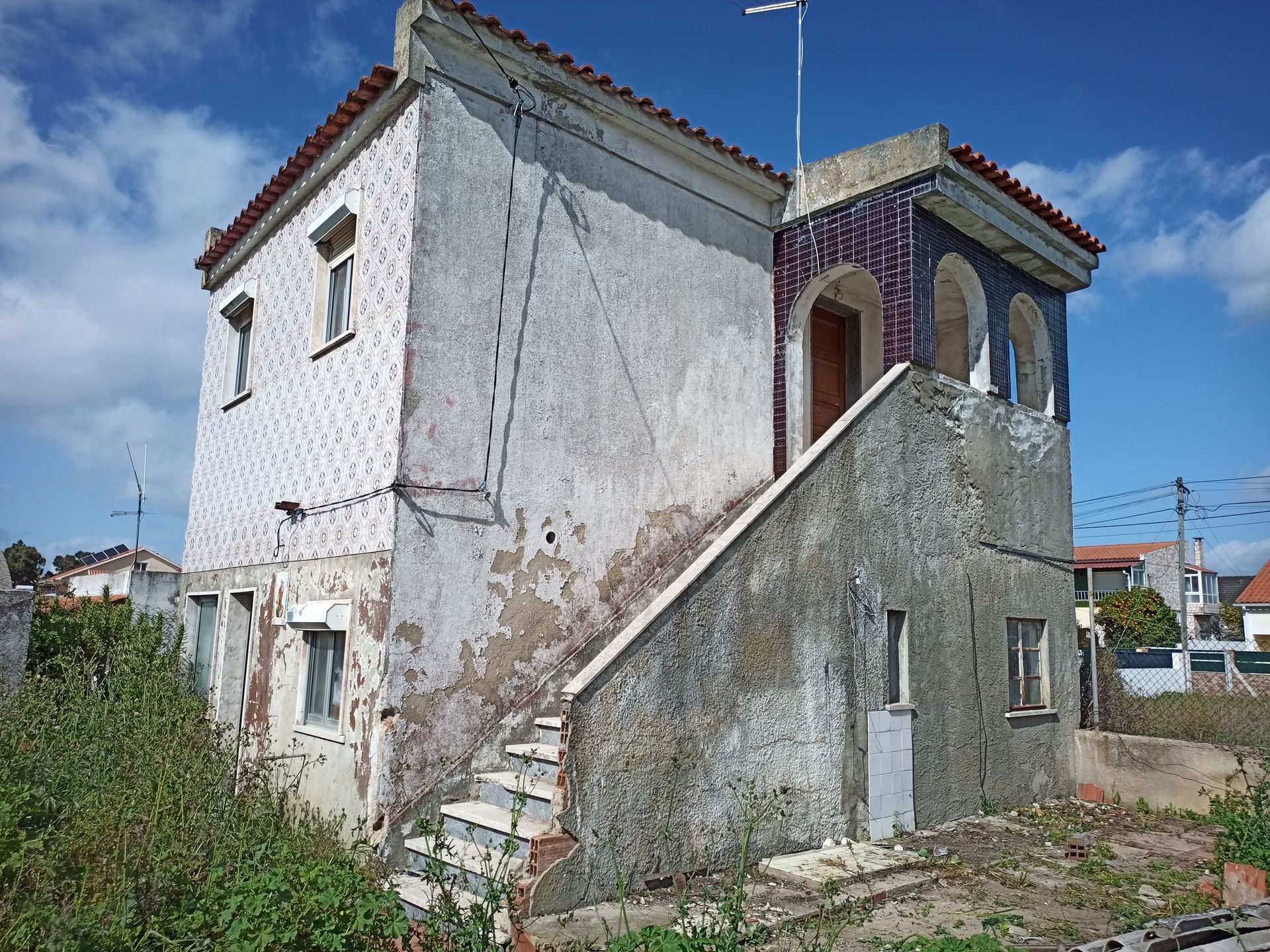 Prédio de dois andares com fachada desgastada, escada externa, estuque descascado e molduras de janelas em arco.