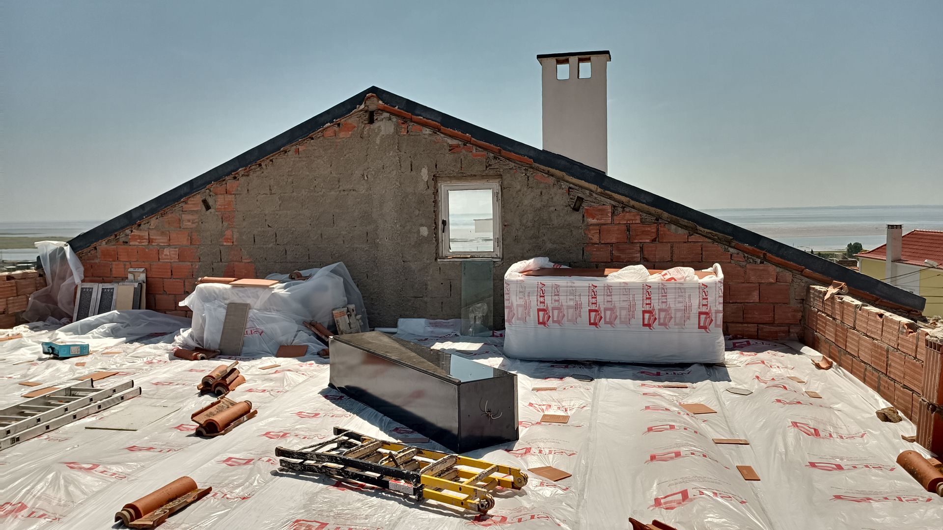 Construção de telhado: tijolos, isolamento, janela, chaminé e materiais de construção em um dia ensolarado.