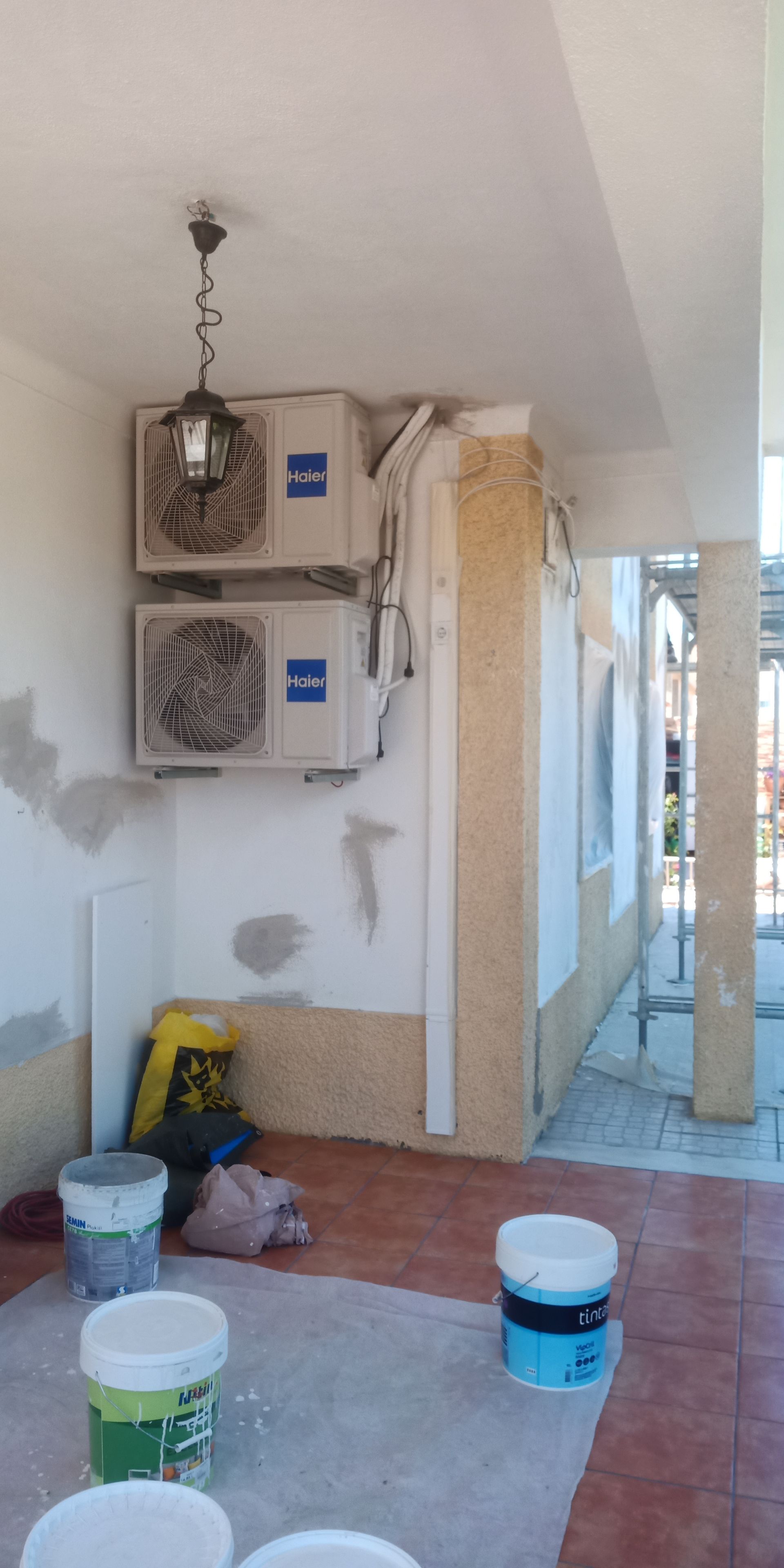Duas unidades de ar condicionado em uma parede em construção, com baldes de tinta e entulho no chão.