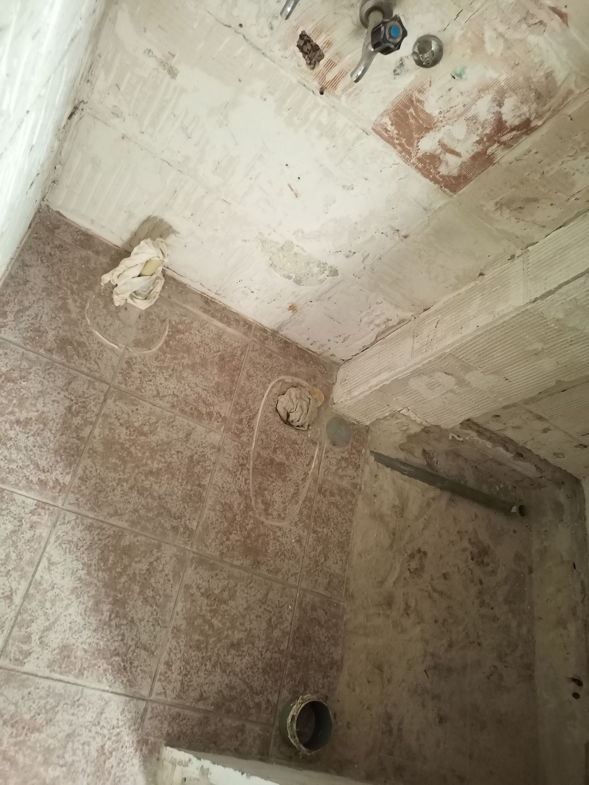 Chuveiro com azulejos marrons, teto e acessórios danificados.