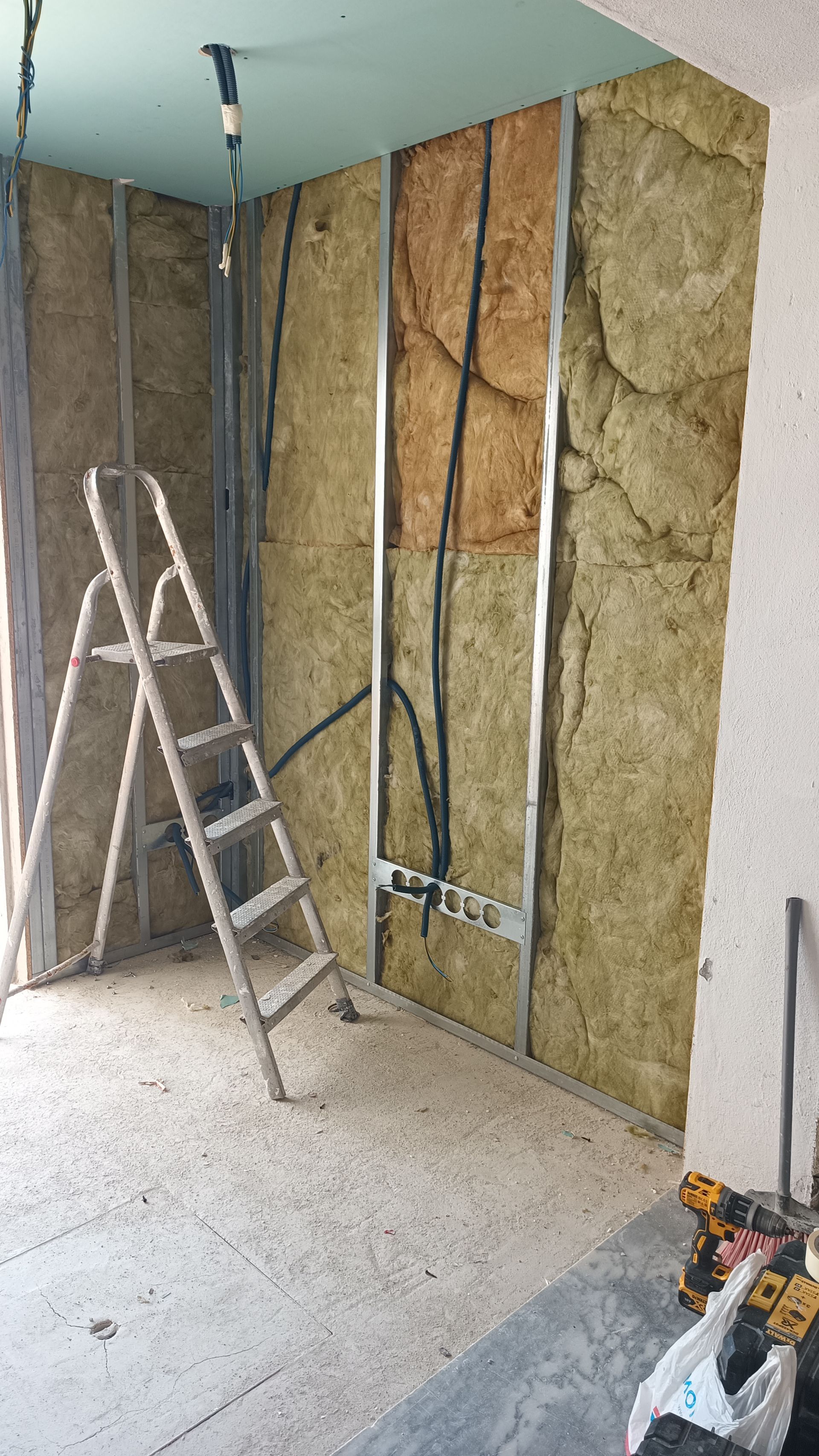 Parede interna em construção com isolamento, vigas, fios e escada.