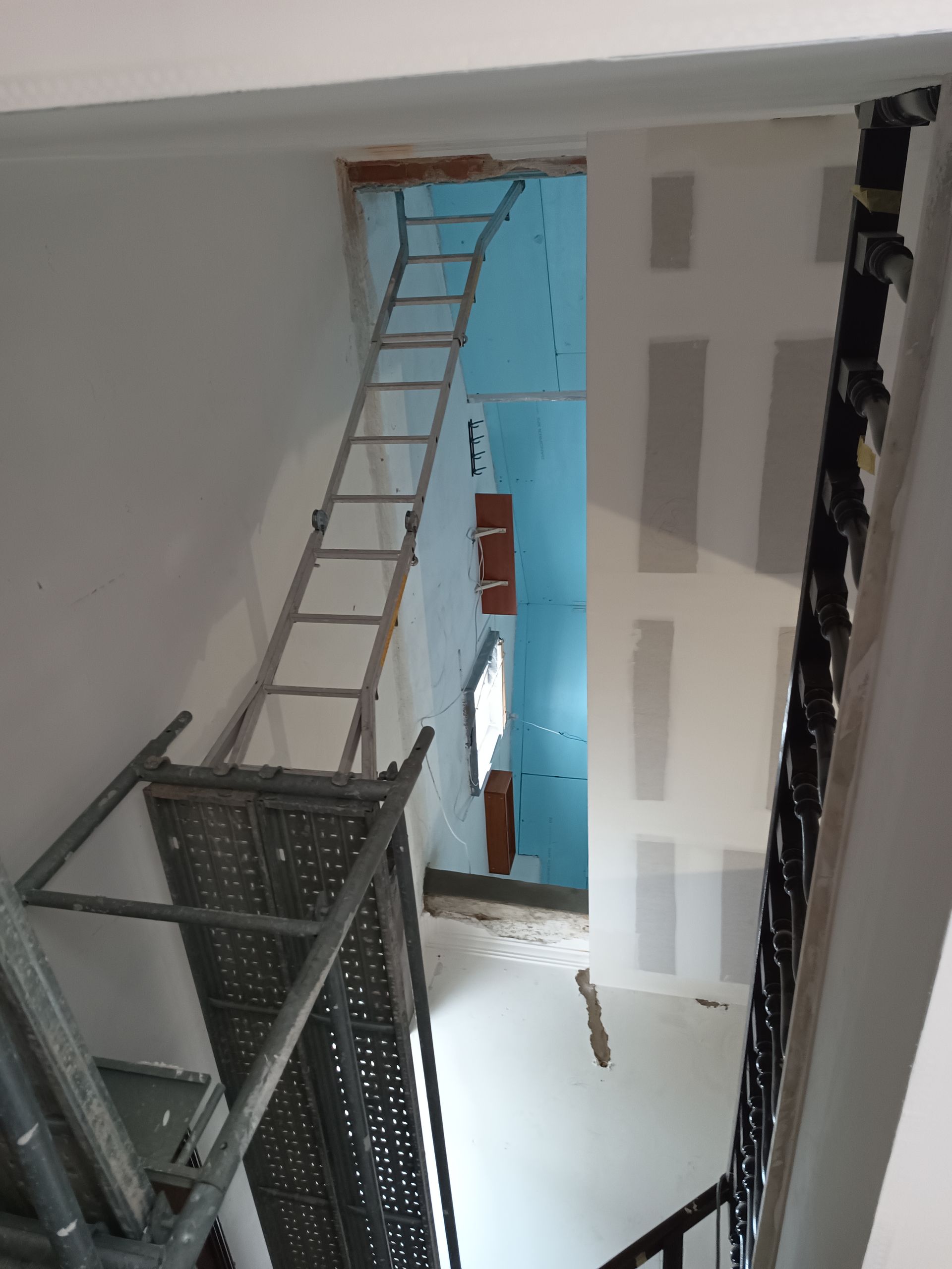 Escada e andaimes na caixa de escada durante a reforma, com a parede de gesso visível.
