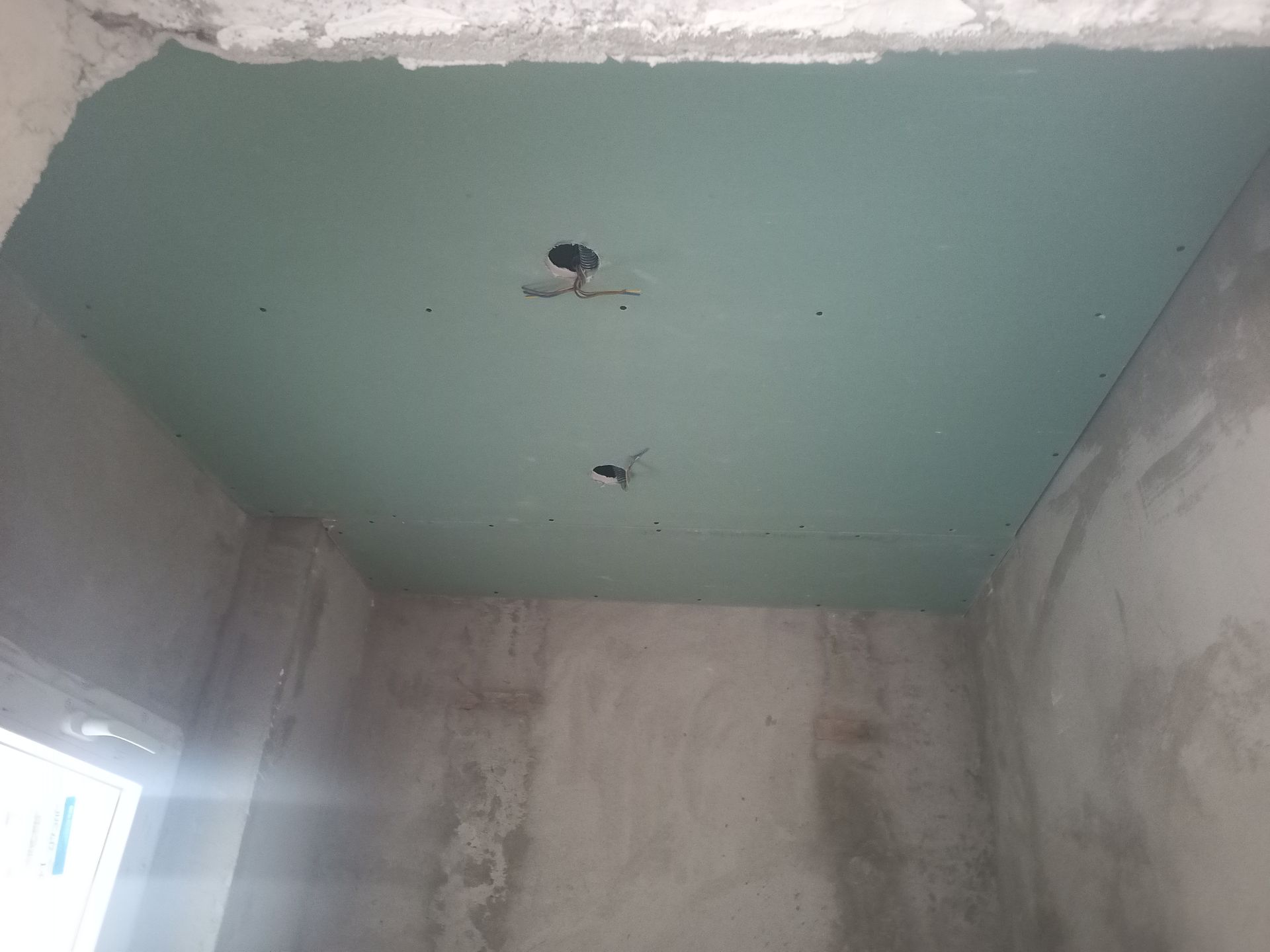 Teto com drywall verde, furos para luminárias e paredes de concreto inacabadas.