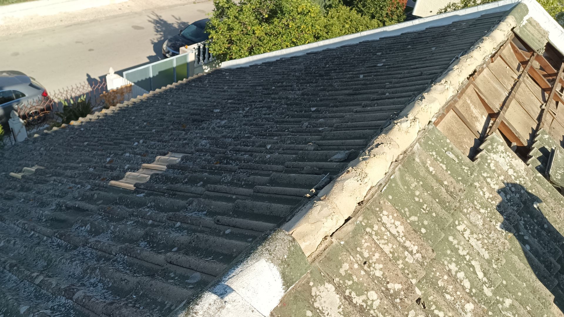 Vista aproximada de um telhado antigo e acinzentado com telhas texturizadas.