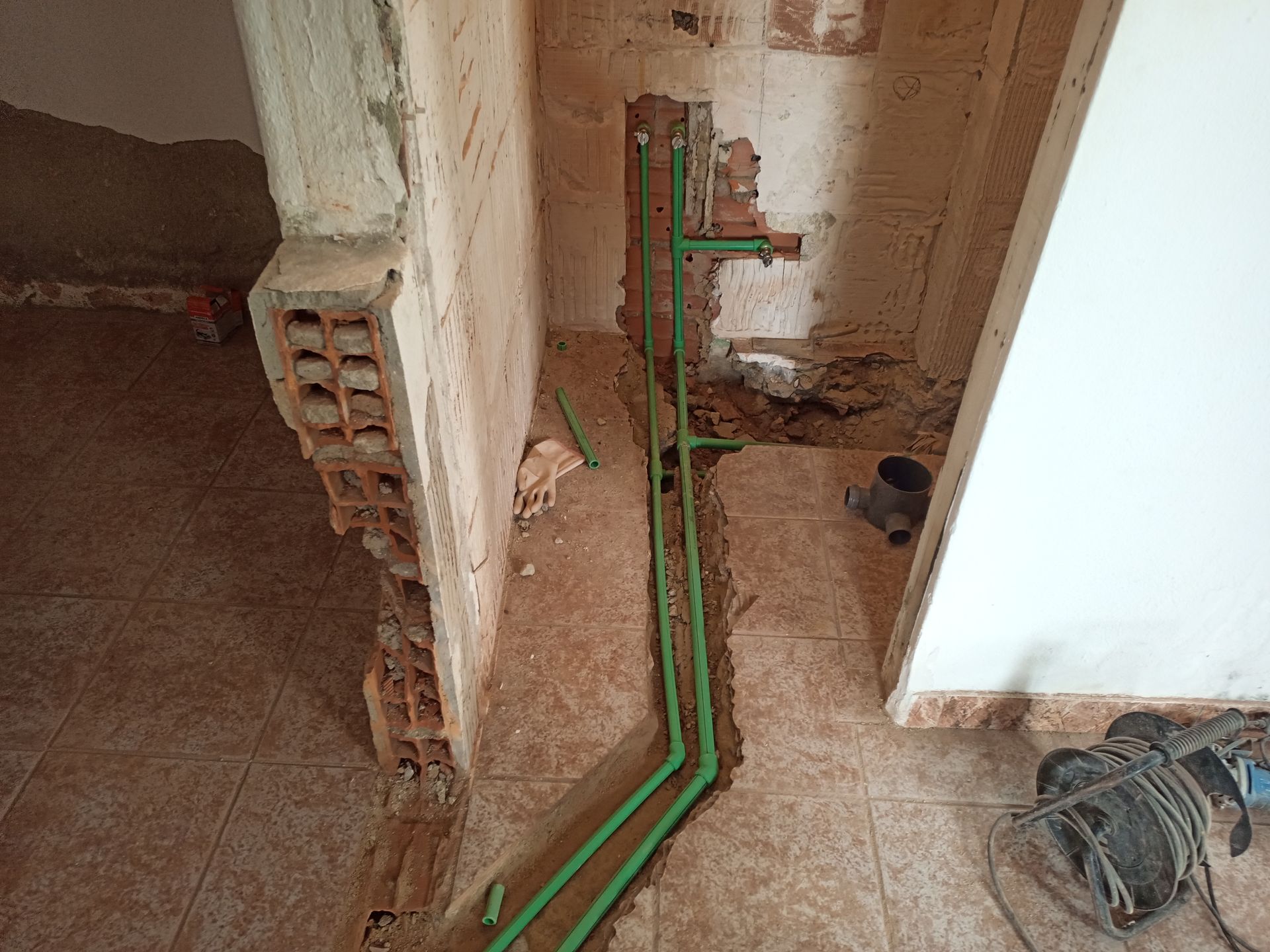 Tubos verdes em uma vala ao longo de uma parede, construção em andamento.