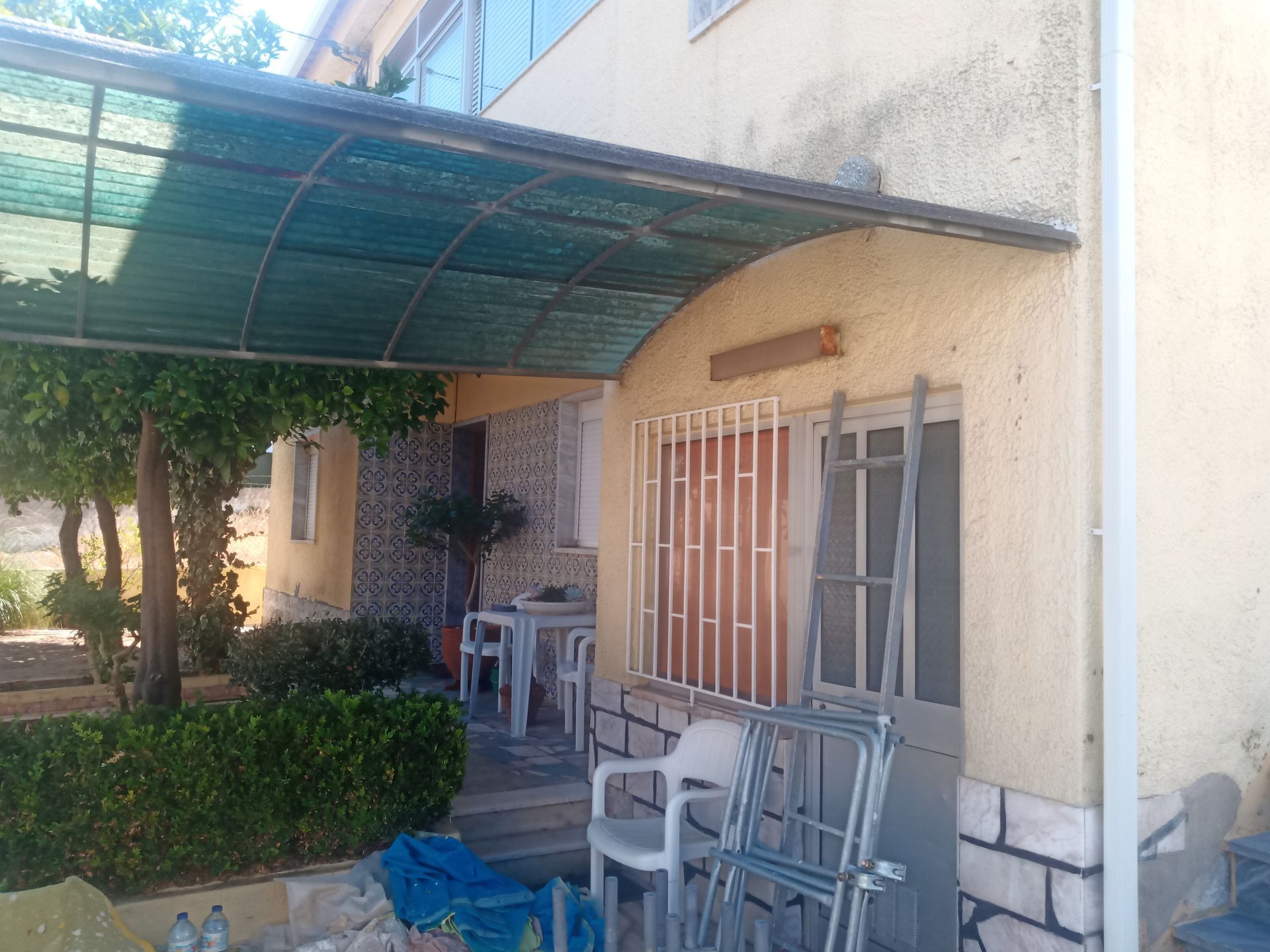 Exterior de uma casa com varanda coberta. Cadeiras e mesa são visíveis.