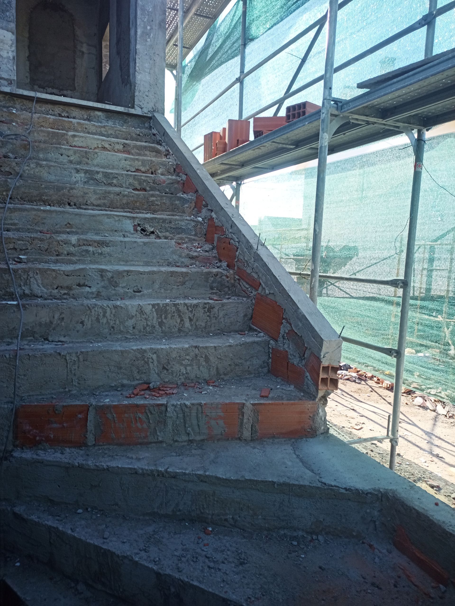 Escada de concreto em construção com detalhes em tijolo e andaimes.