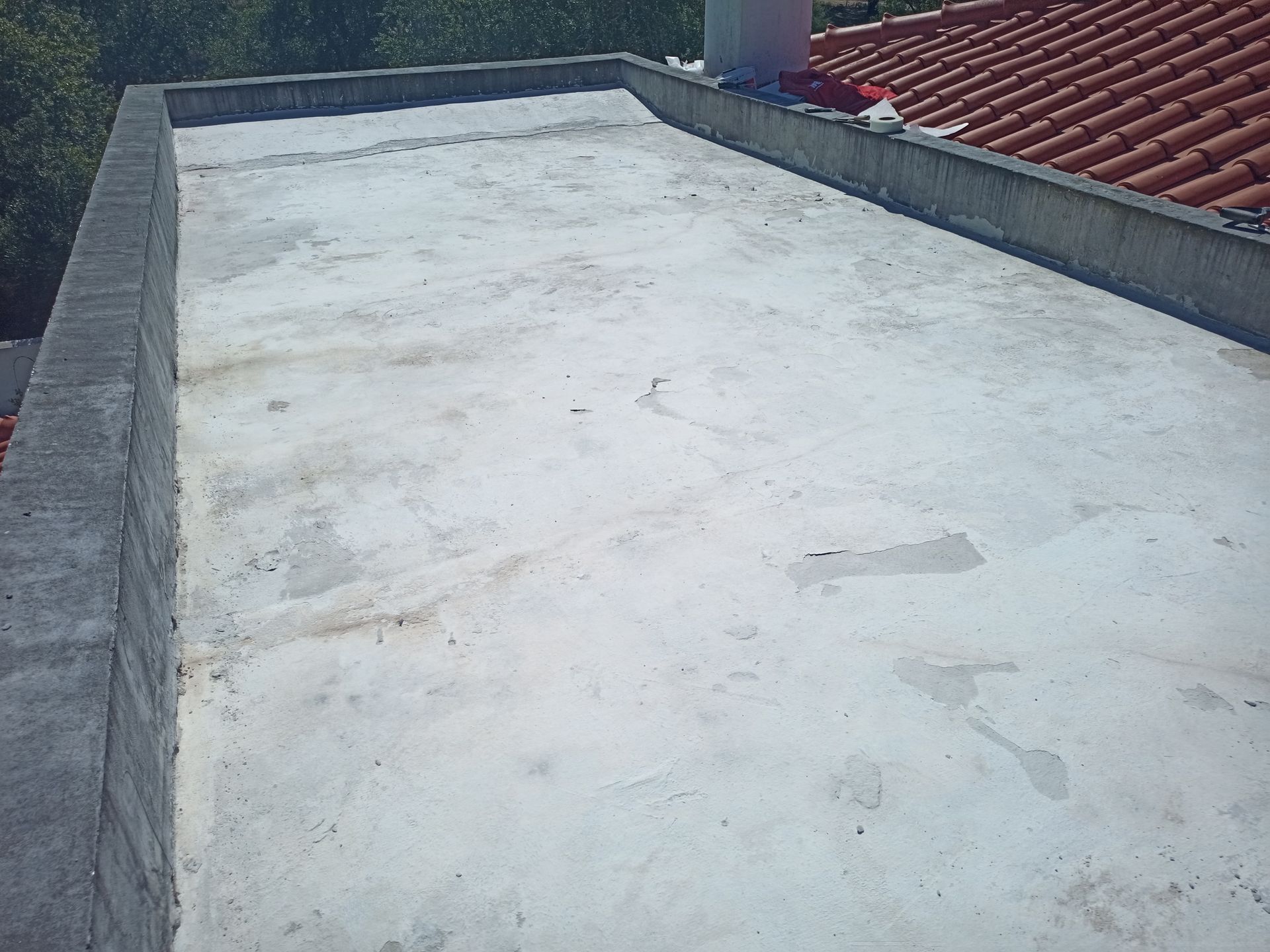 Telhado plano de concreto cinza com um muro de contenção baixo. Telhado de telha vermelha visível à direita.