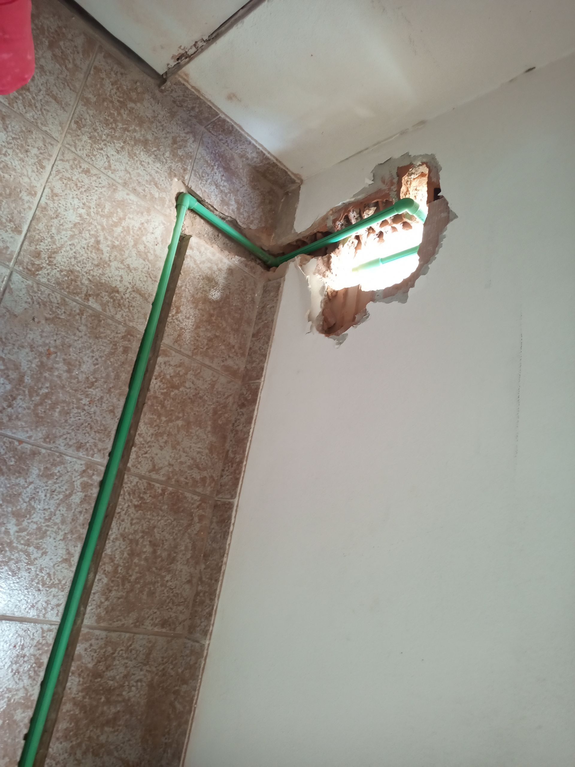 Tubos verdes saindo de uma parede, percorrendo o piso de azulejos. Buraco na parede.