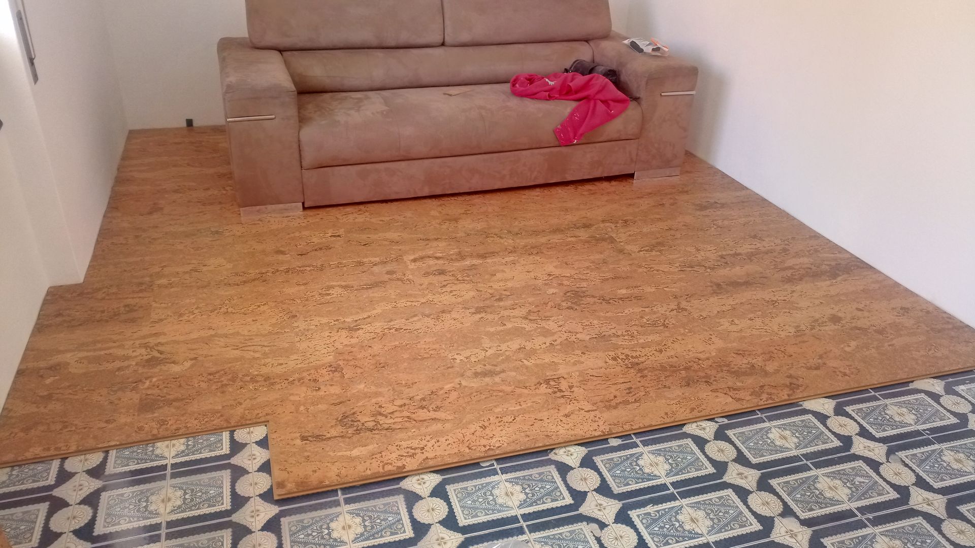 Instalação de piso de cortiça em um cômodo, com sofá e carpete parcialmente visíveis.