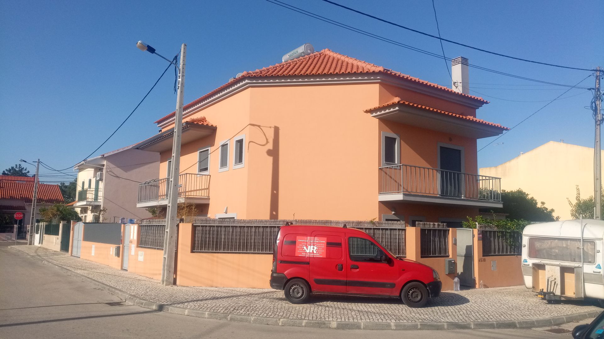Prédio laranja de dois andares com uma van vermelha estacionada em frente em um dia ensolarado.