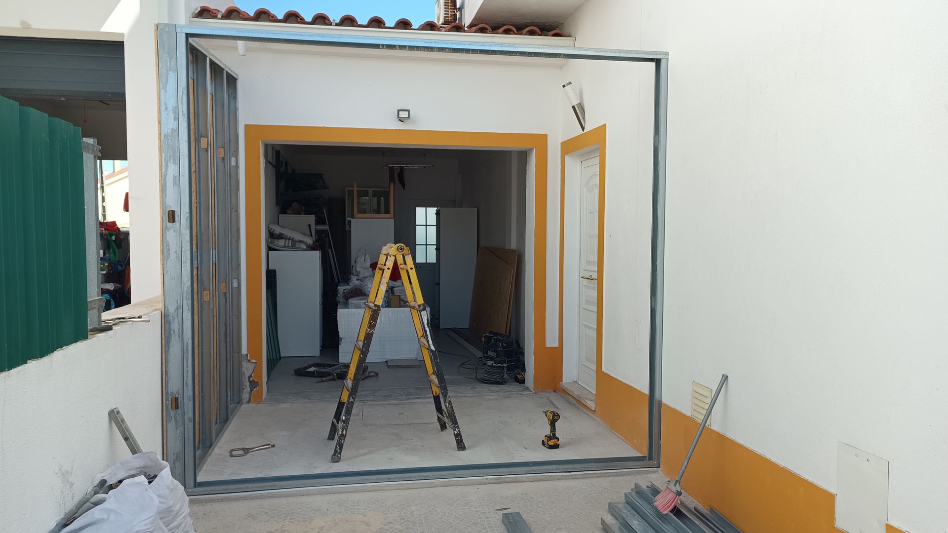 Vista exterior de um edifício em construção, com caixilhos de portas abertos e uma escada no interior.