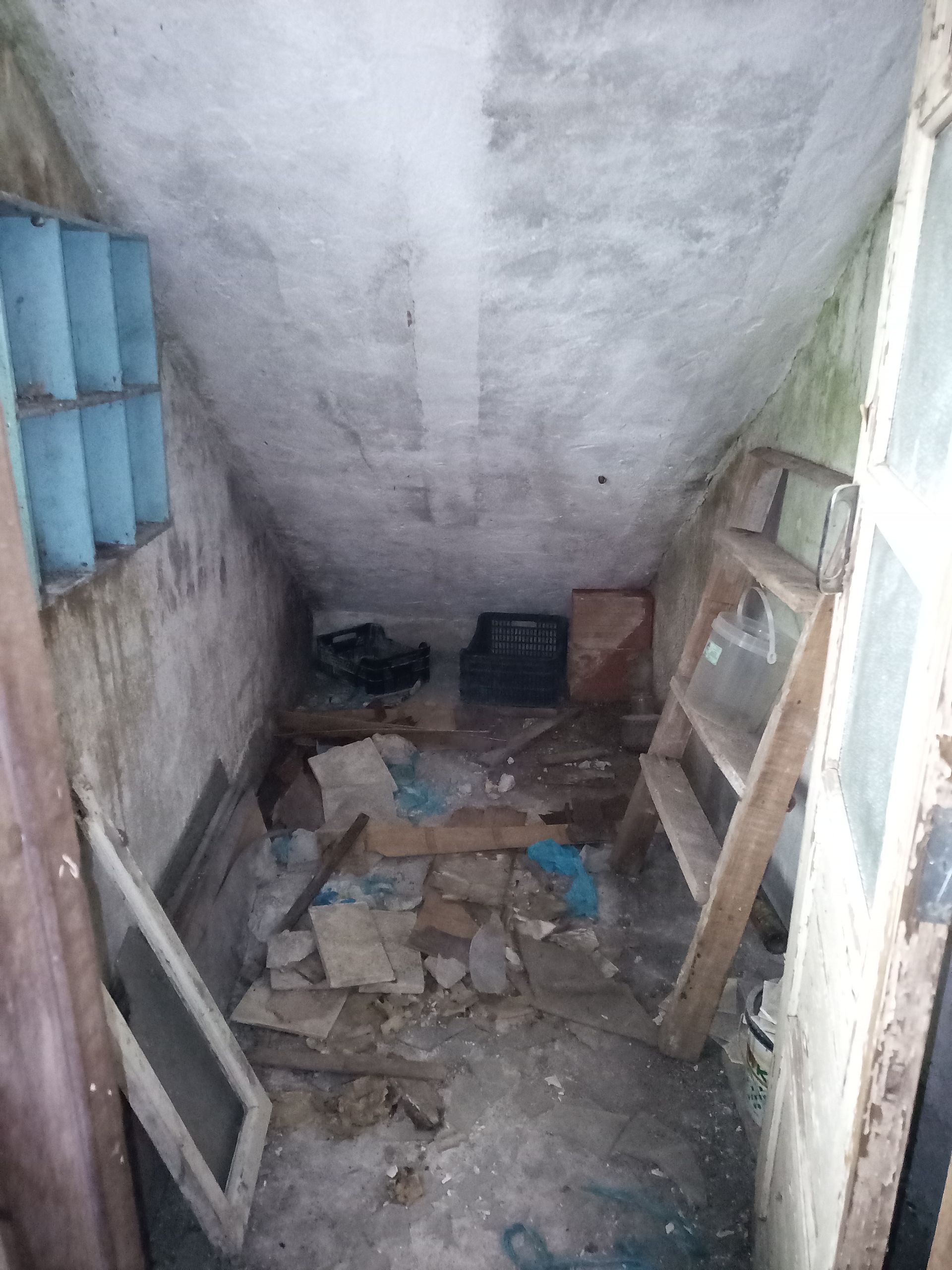 Espaço de armazenamento estreito e desorganizado, com entulho e uma escada.