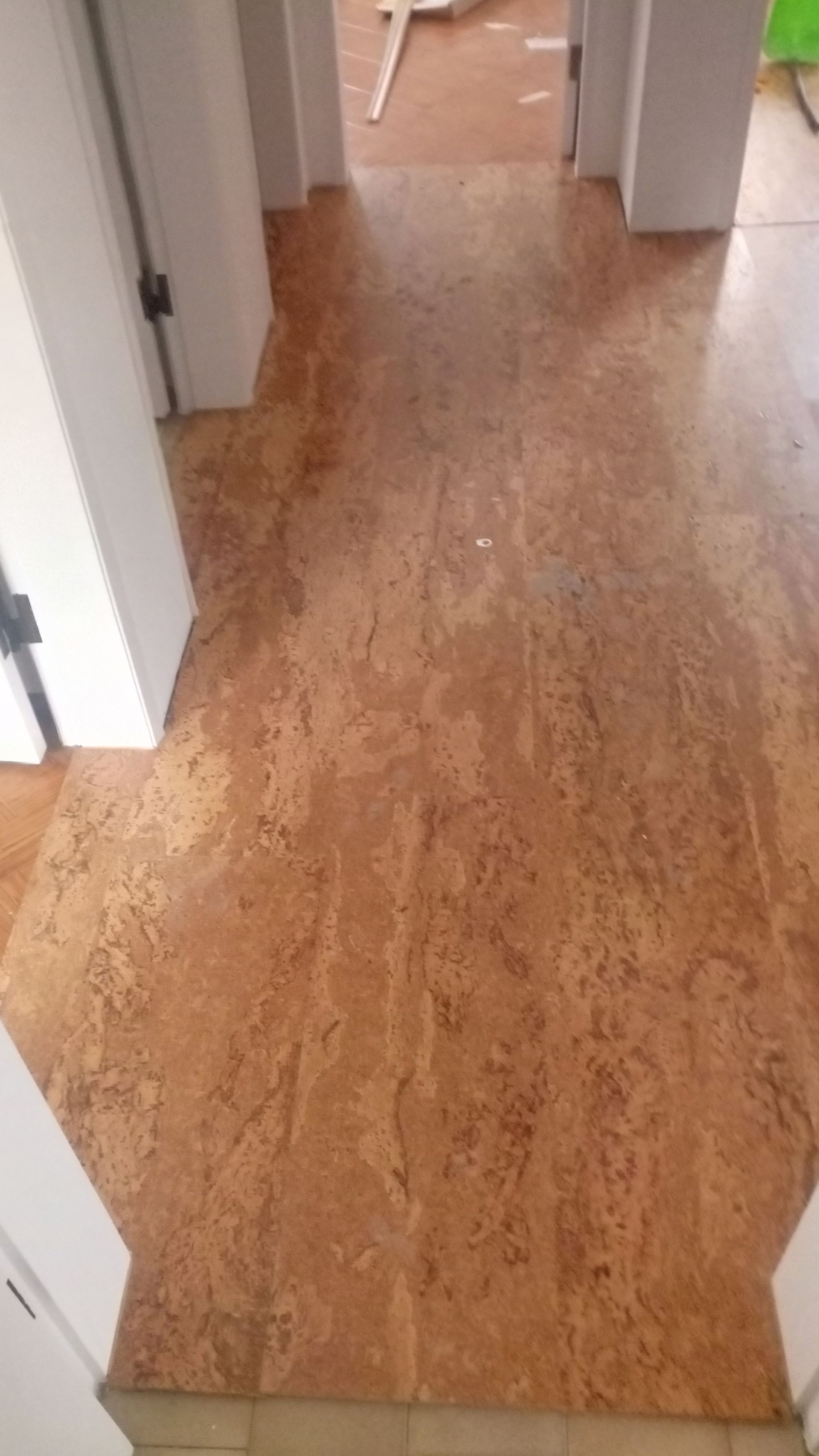 Piso de cortiça no corredor, com padrão mesclado em tons de bege e marrom, e batentes de porta brancos.