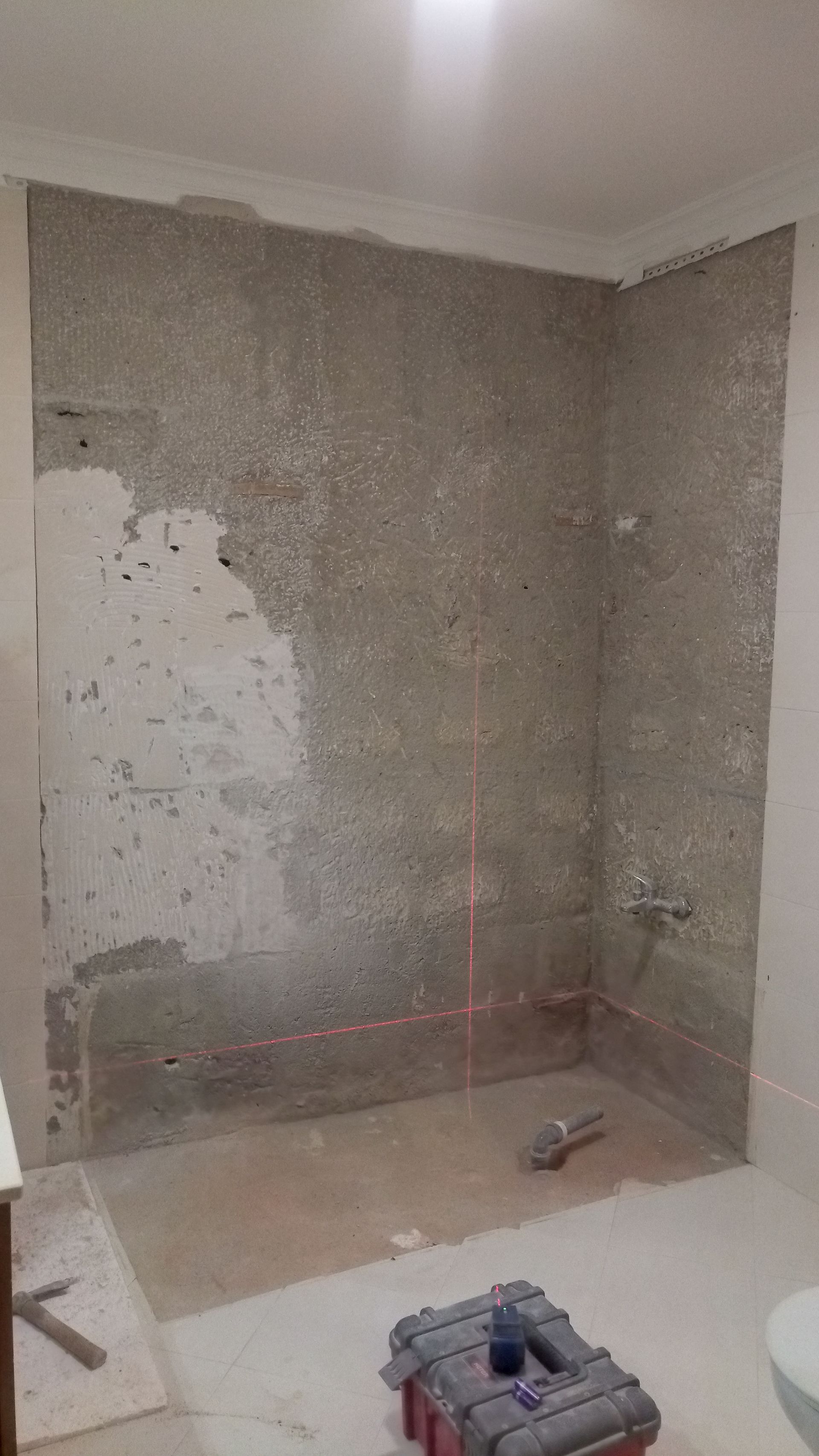 Área do chuveiro do banheiro em construção; paredes de concreto cinza com linhas vermelhas de nível a laser.