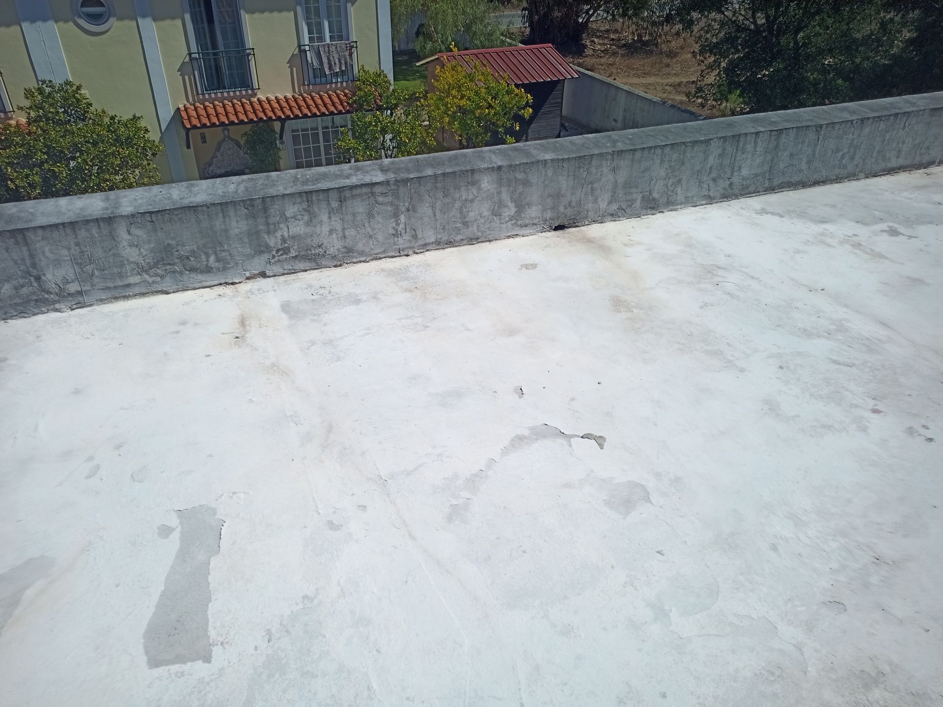 Um telhado de concreto com um muro baixo, edifícios parcialmente visíveis e árvores ao fundo.