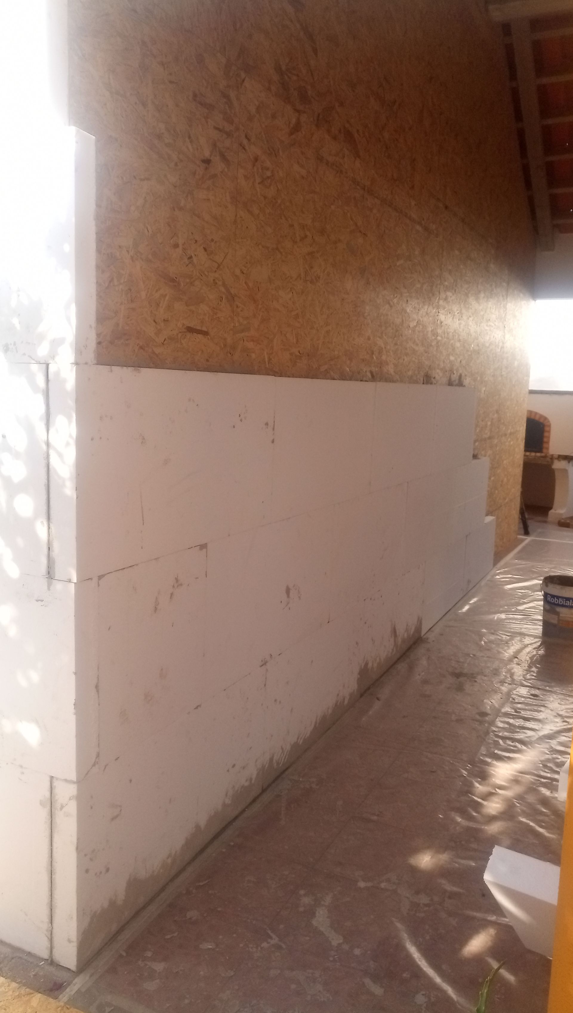 Construção de parede externa com isolamento de espuma de cor clara e painéis de madeira, em um ambiente externo bem iluminado.