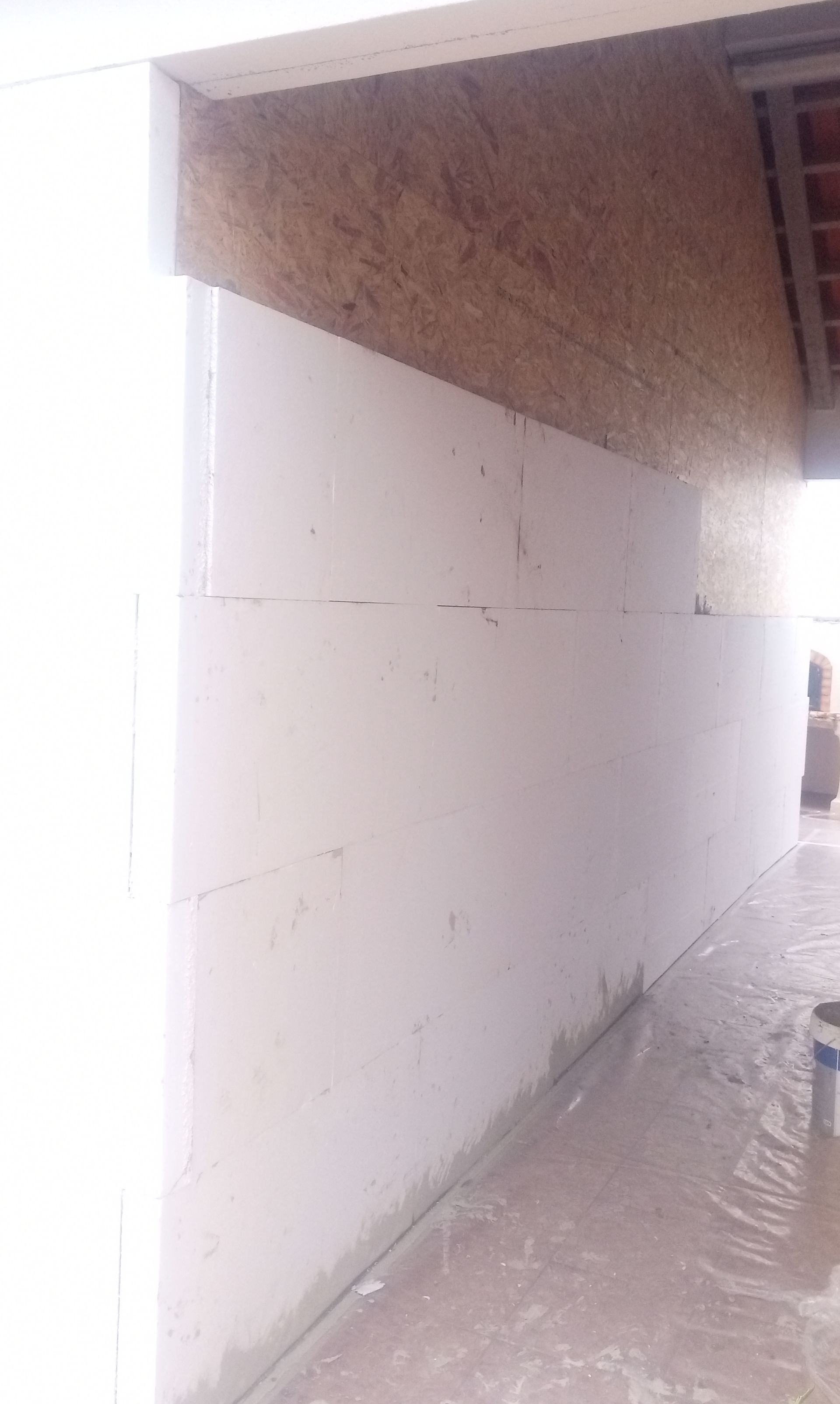 Parede de estuque branco em construção com painéis de madeira expostos acima.