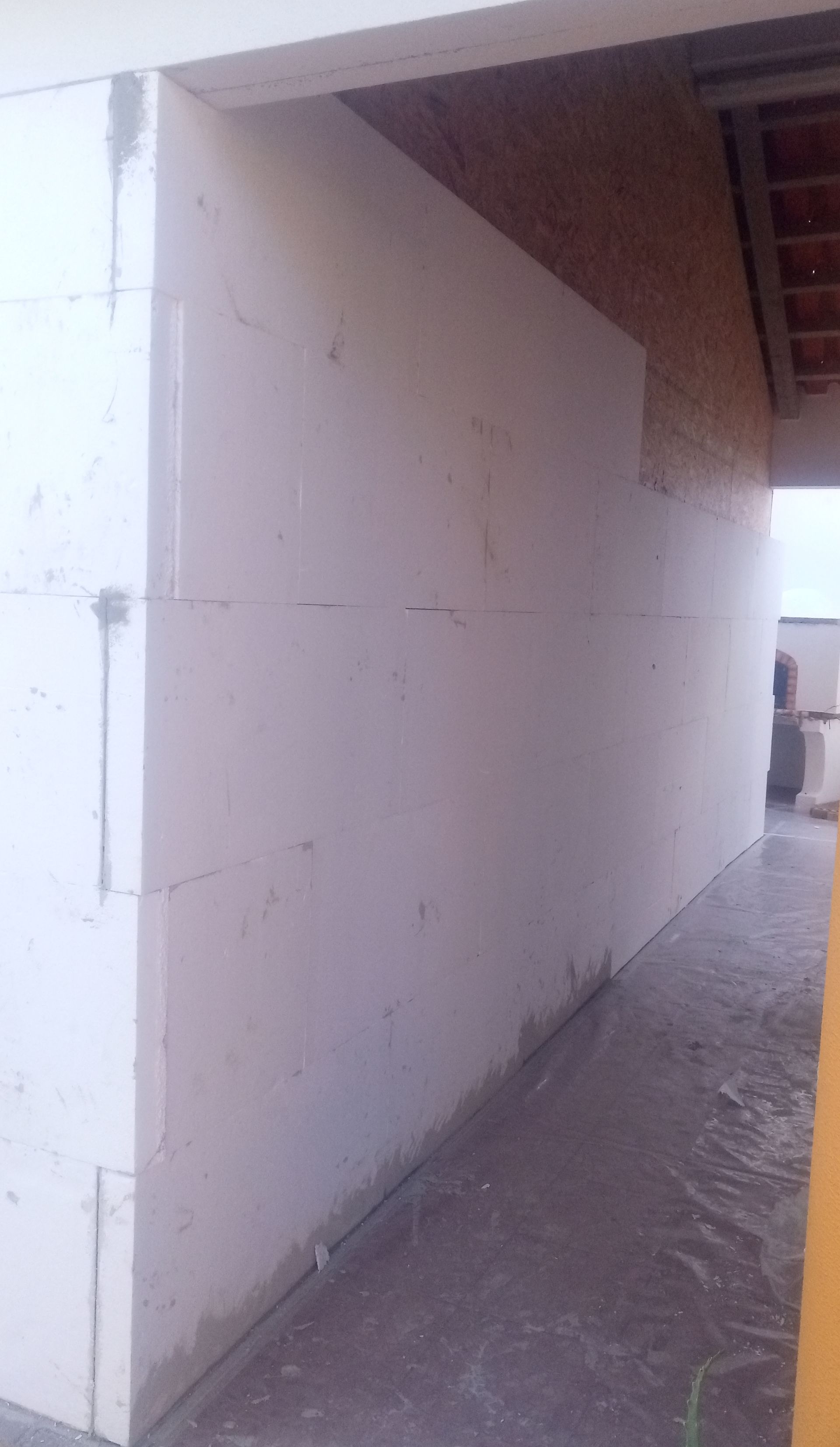 Parede construída com blocos de espuma branca. Placas de partículas marrons e um piso escuro também estão presentes.