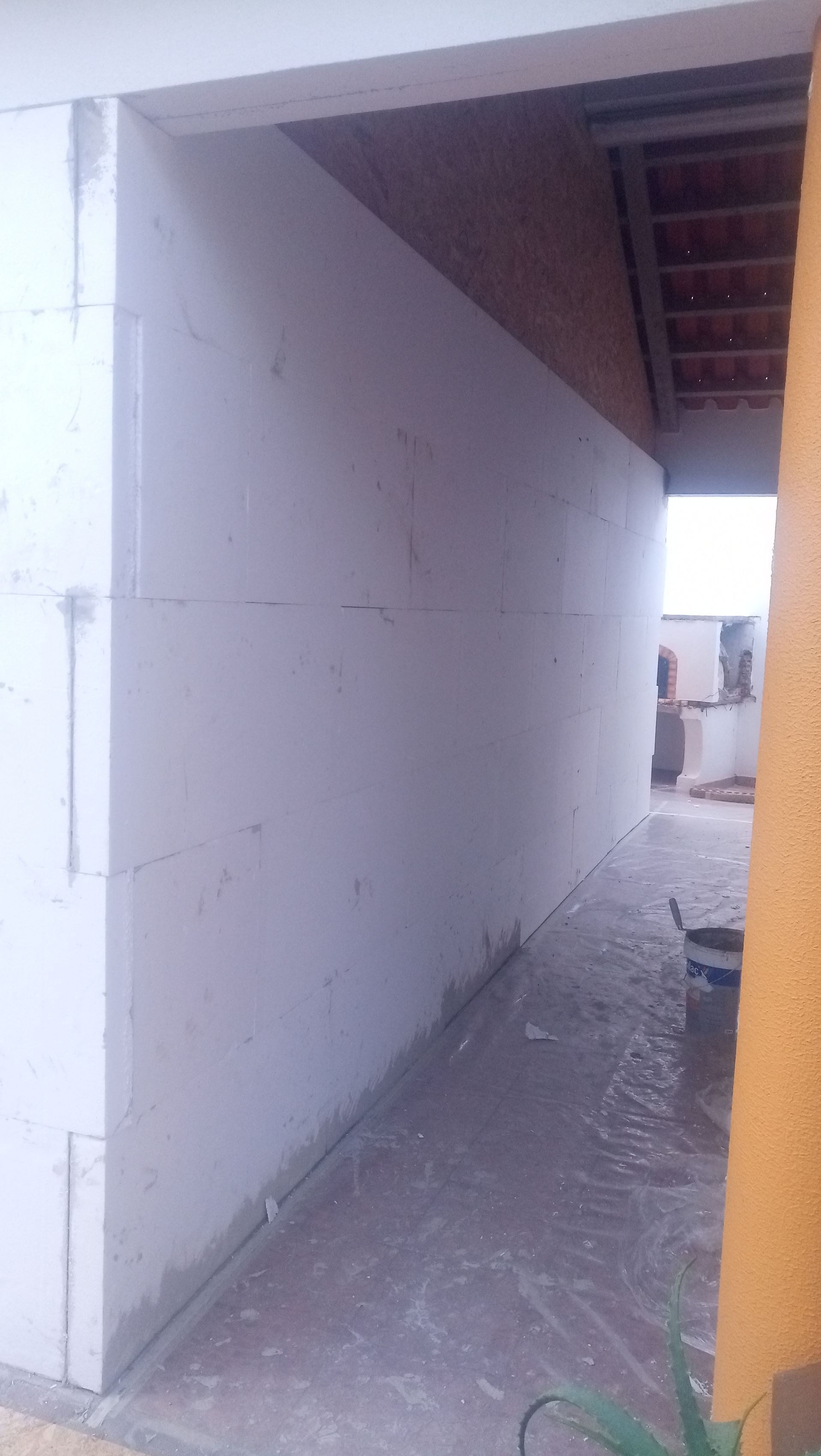 Blocos de construção brancos formando uma passagem estreita, aberta para uma área externa com um telhado de telhas vermelhas visível.