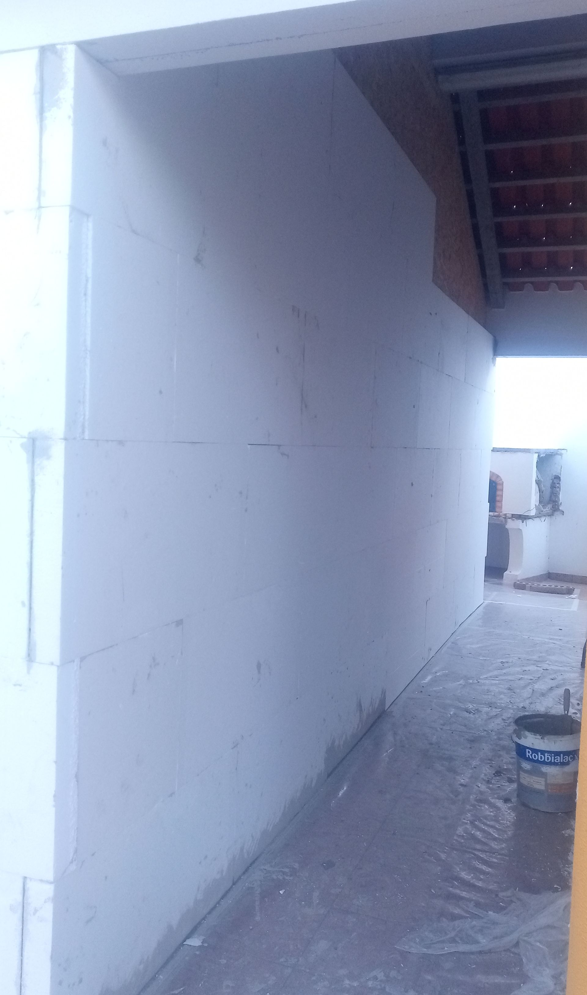 Construção interior com paredes brancas, piso inacabado, porta e balde.