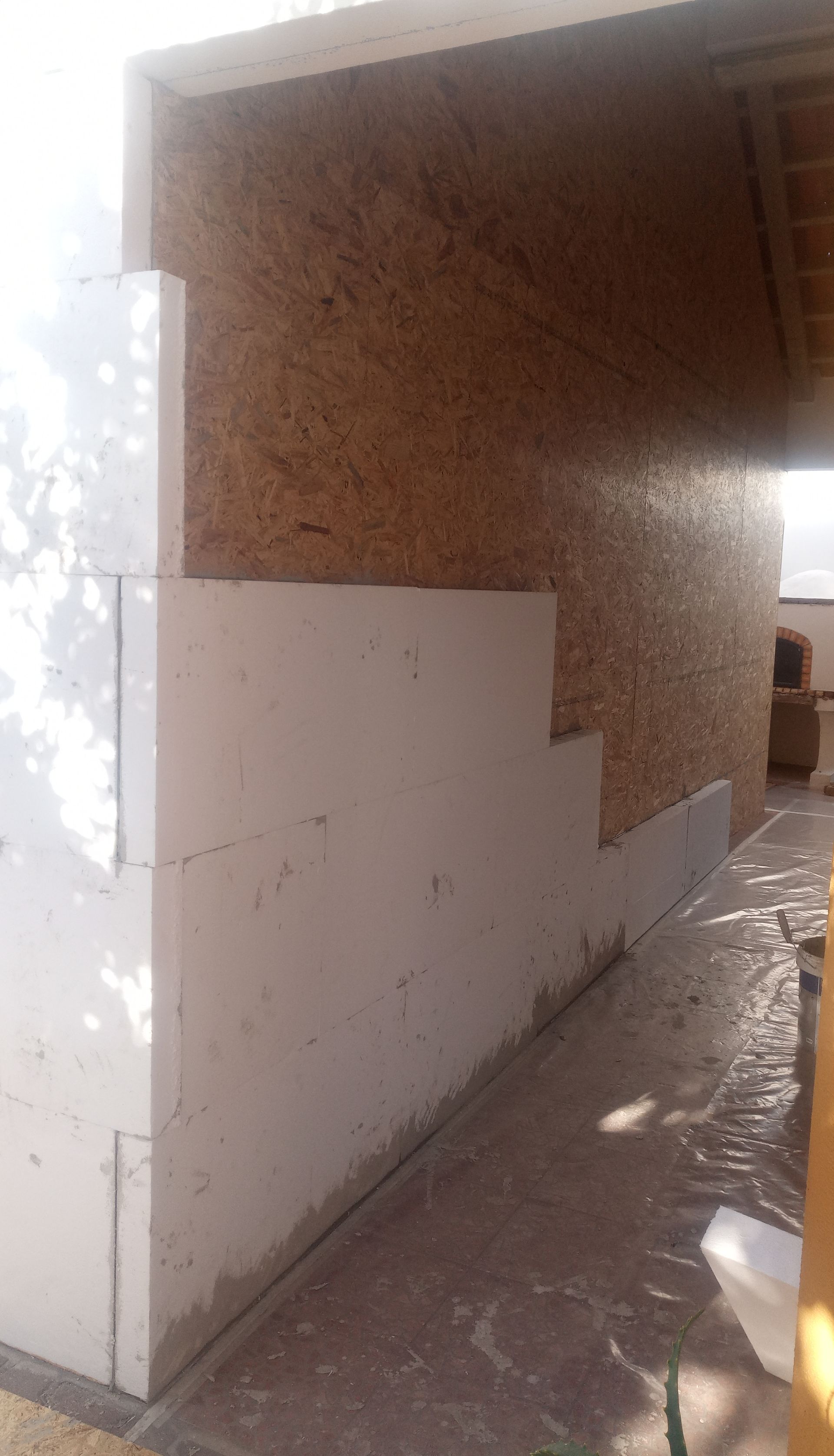 Blocos de isolamento de espuma branca sendo instalados em uma parede, ao lado de um painel de madeira.