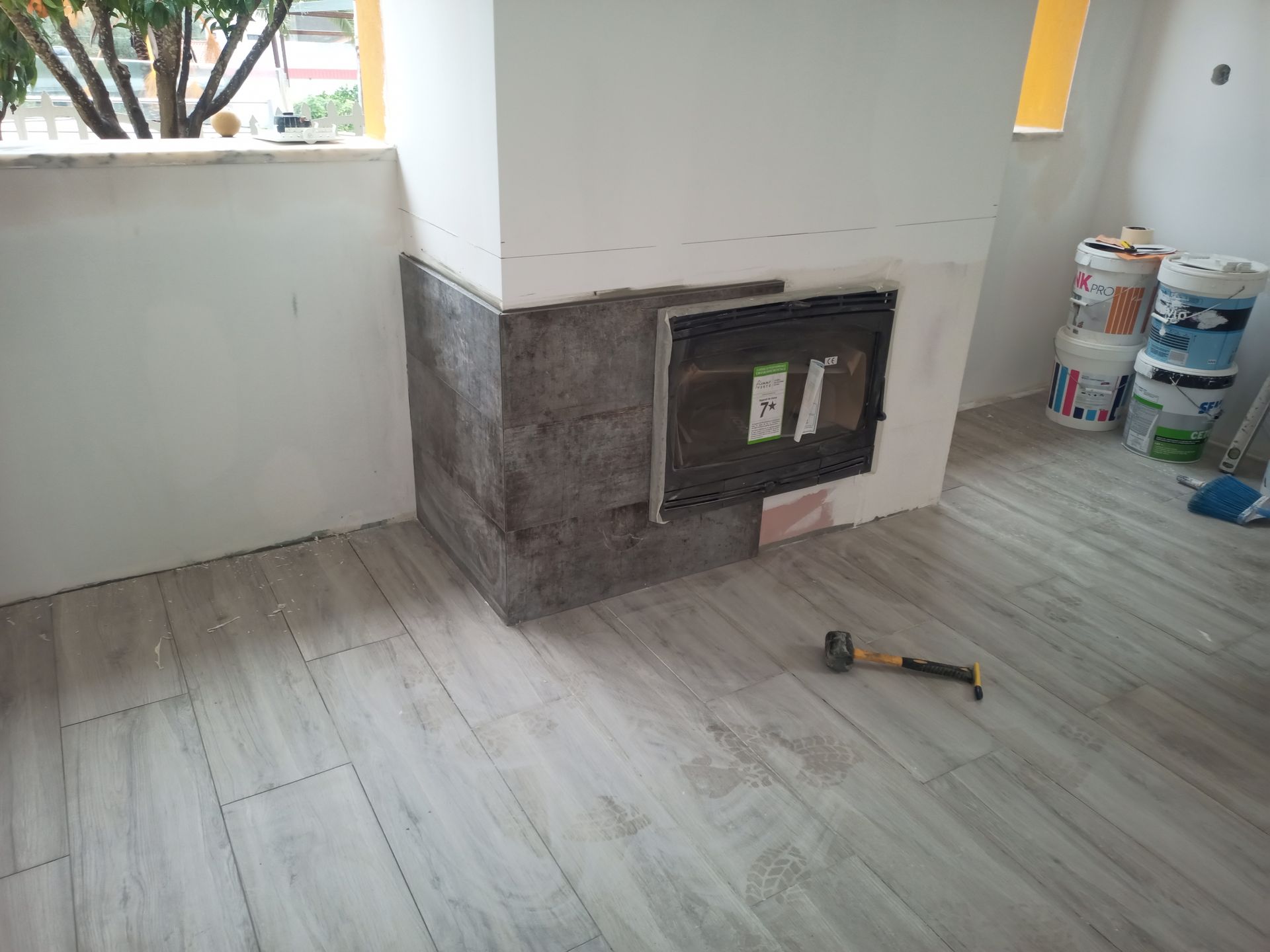 Lareira em construção, parcialmente revestida com pedra cinza. O piso é de porcelanato que imita madeira clara.