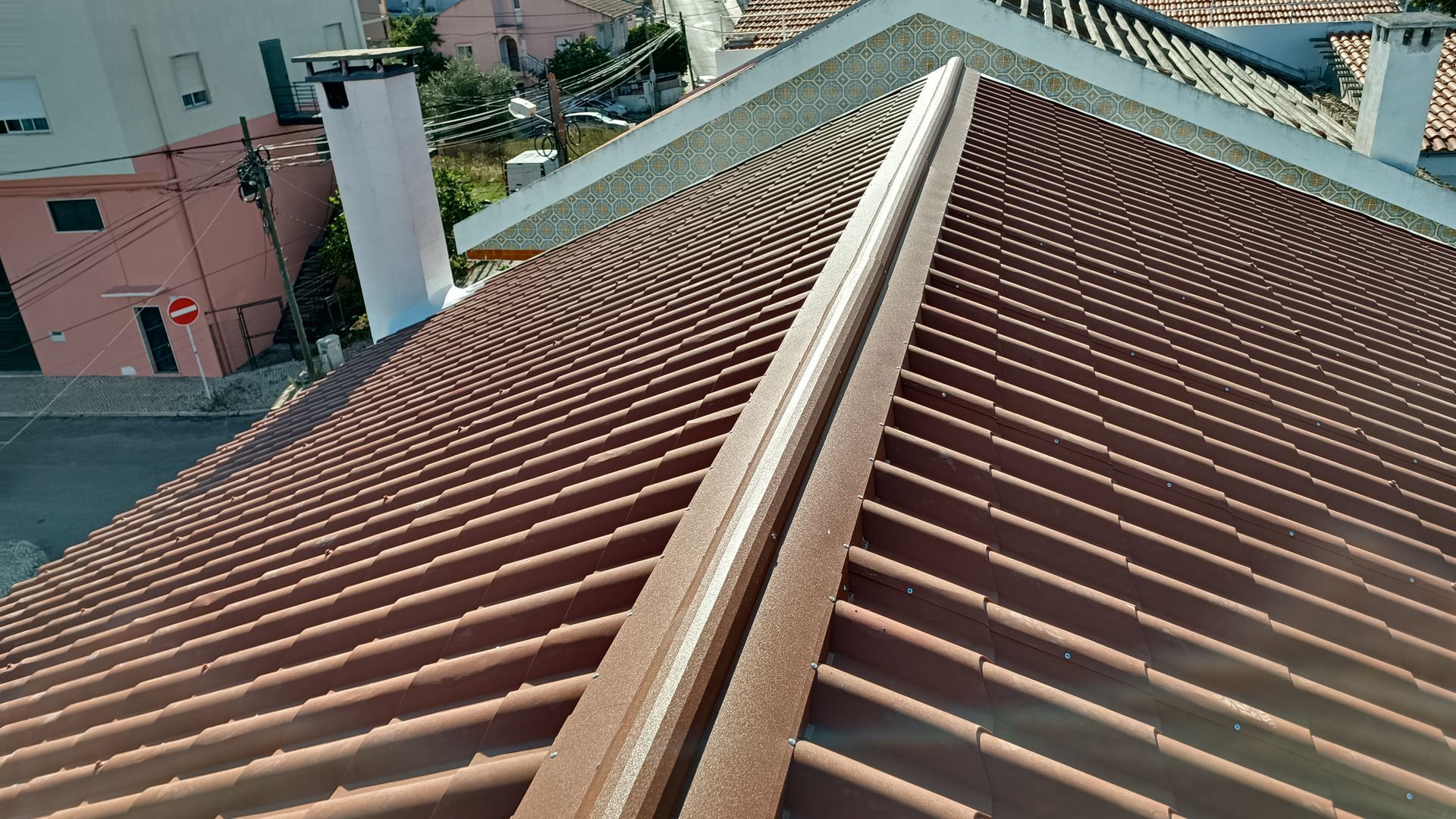 Telhado de telha marrom com cumeeira, com vista para edifícios e rua.