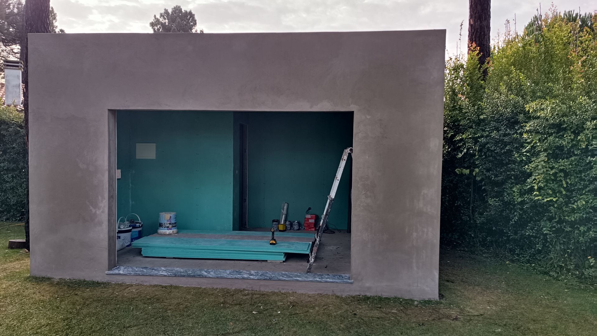 Estrutura de concreto cinza com uma porta aberta, interior com paredes turquesa, em meio a um gramado.