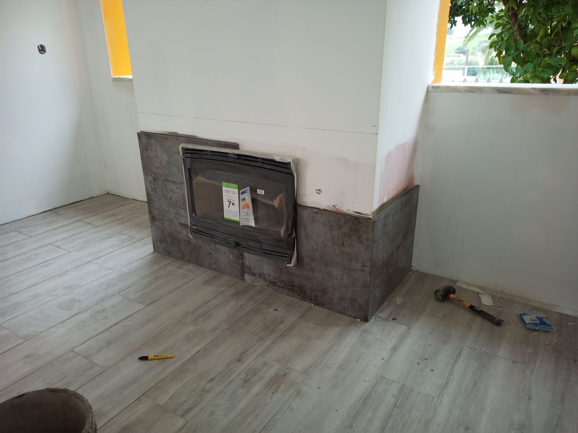 Lareira em construção, revestida com ladrilhos de pedra cinza e piso que imita madeira clara.