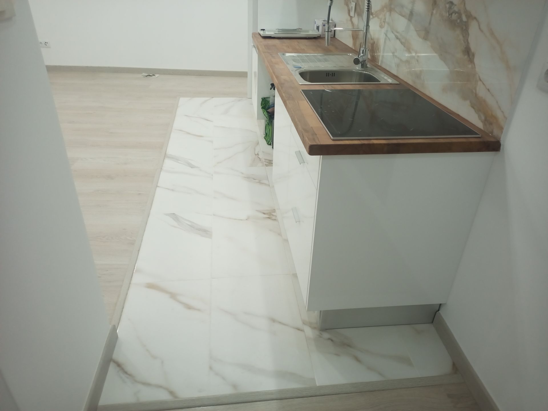 Cozinha pequena com armários brancos, bancada de madeira e piso de mármore.