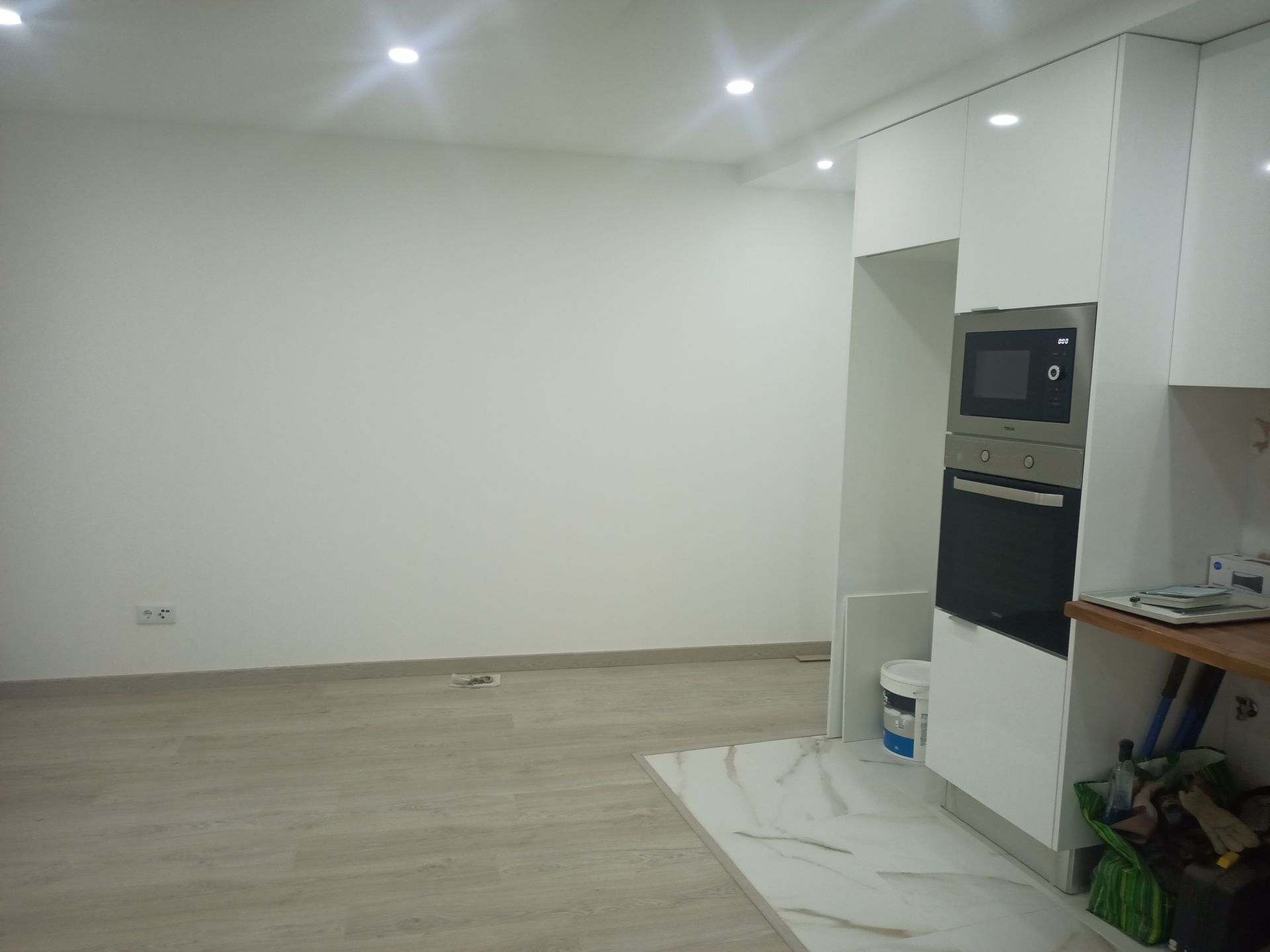 Sala vazia com paredes brancas, forno e micro-ondas embutidos à direita. Piso claro.