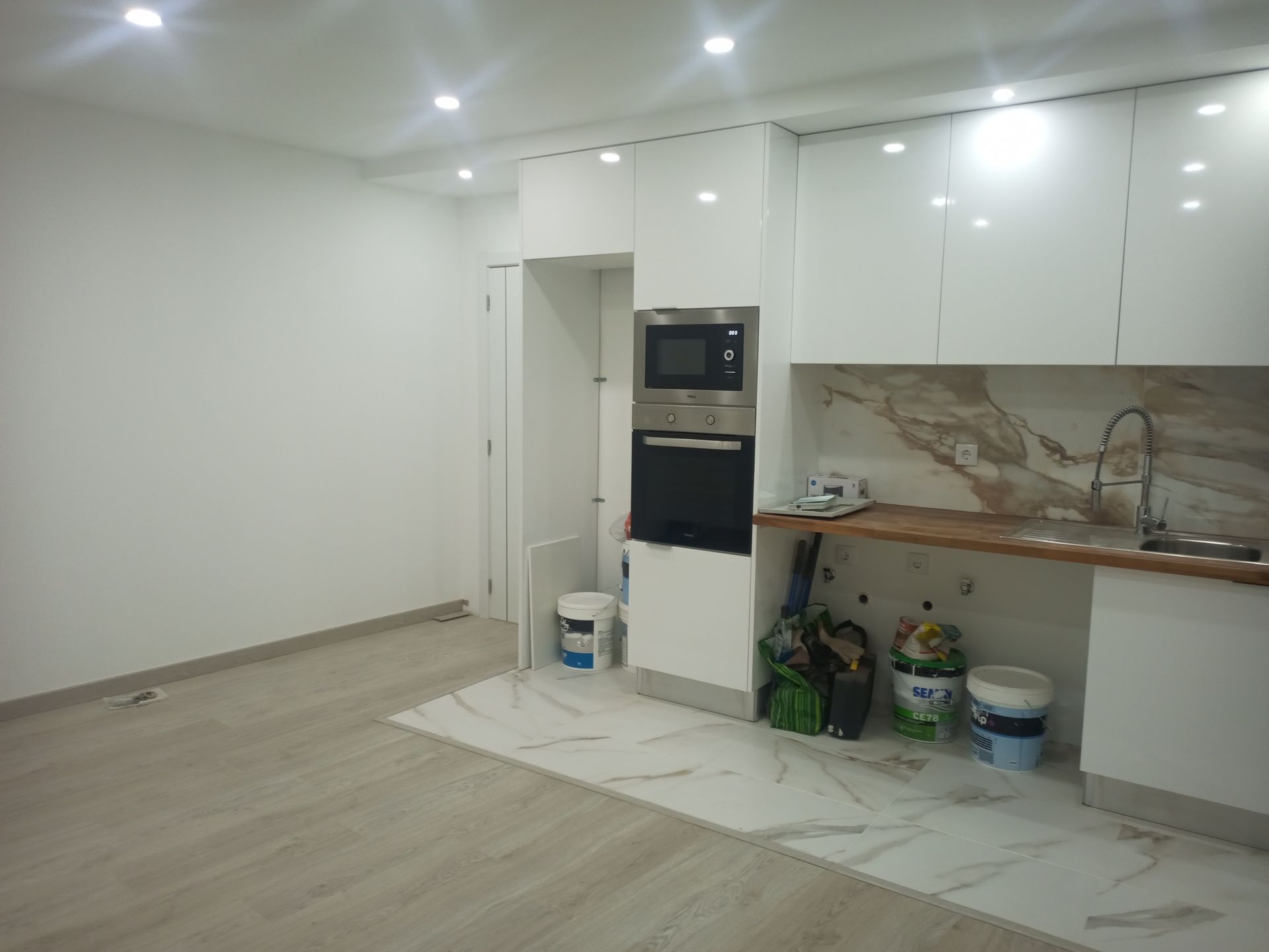 Cozinha moderna em construção com armários brancos, eletrodomésticos e pisos e paredes em tons claros.
