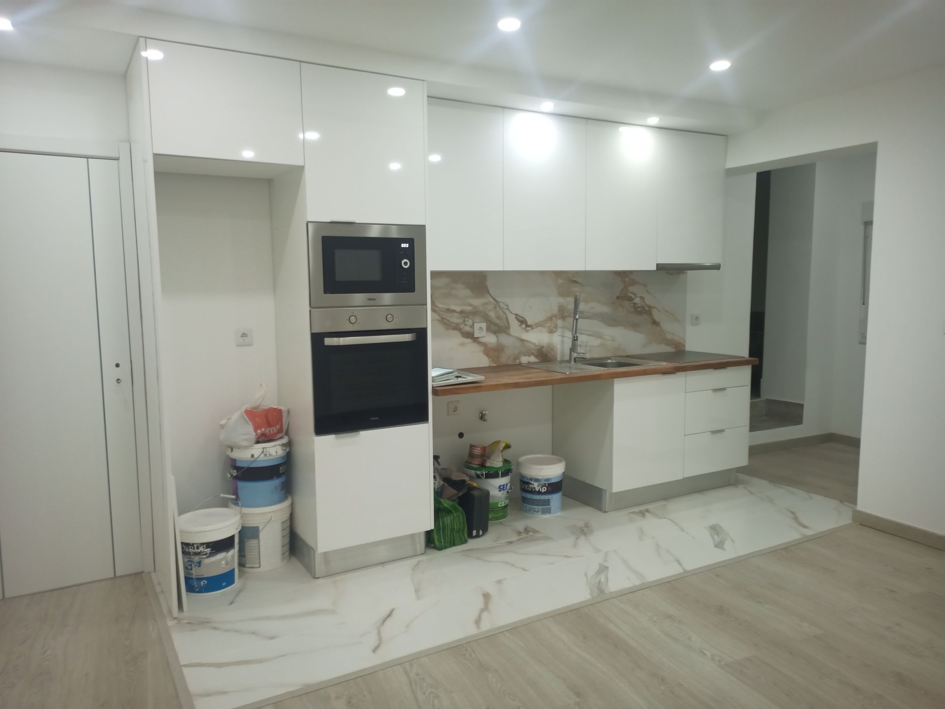 Cozinha moderna branca com eletrodomésticos embutidos, backsplash de mármore e baldes de tinta no chão.
