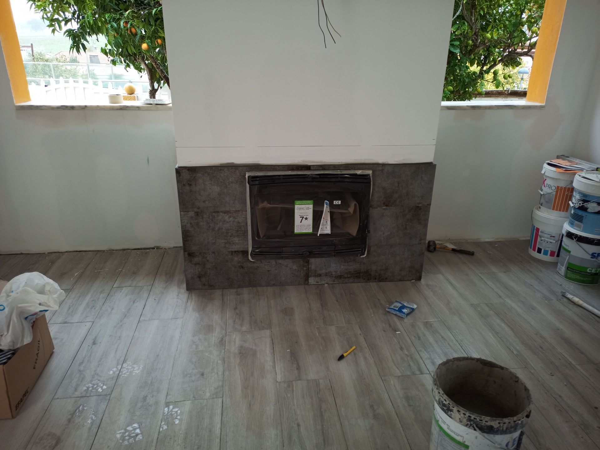 Lareira em construção, cercada por ladrilhos, baldes e janela.