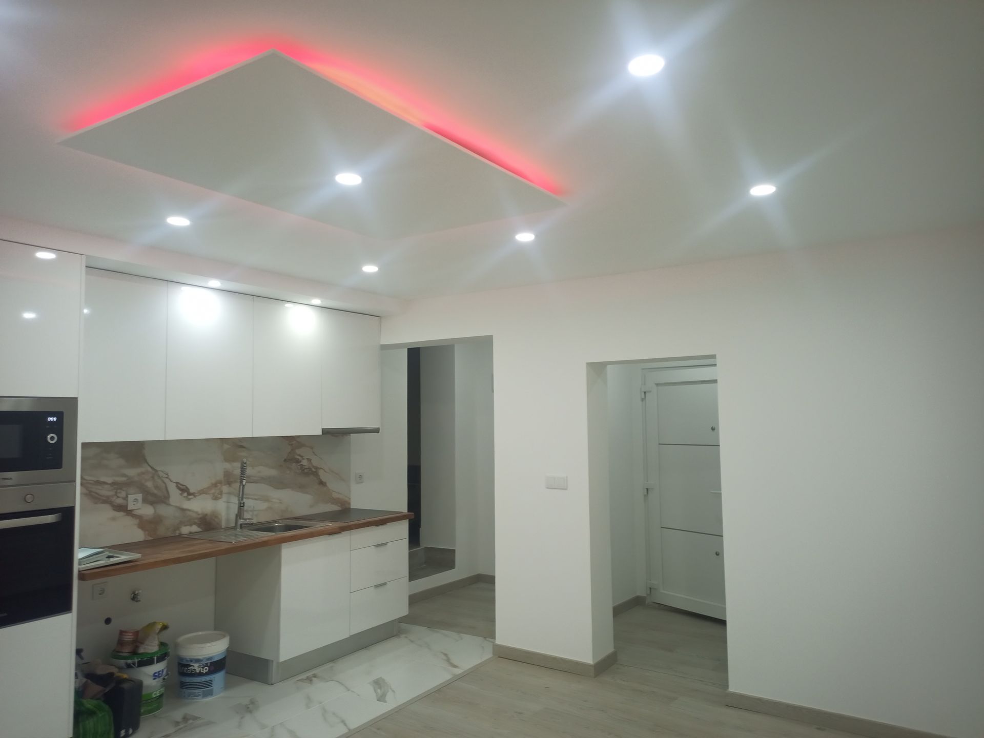 Cozinha moderna branca com backsplash de mármore, iluminação embutida e detalhes em vermelho na iluminação.