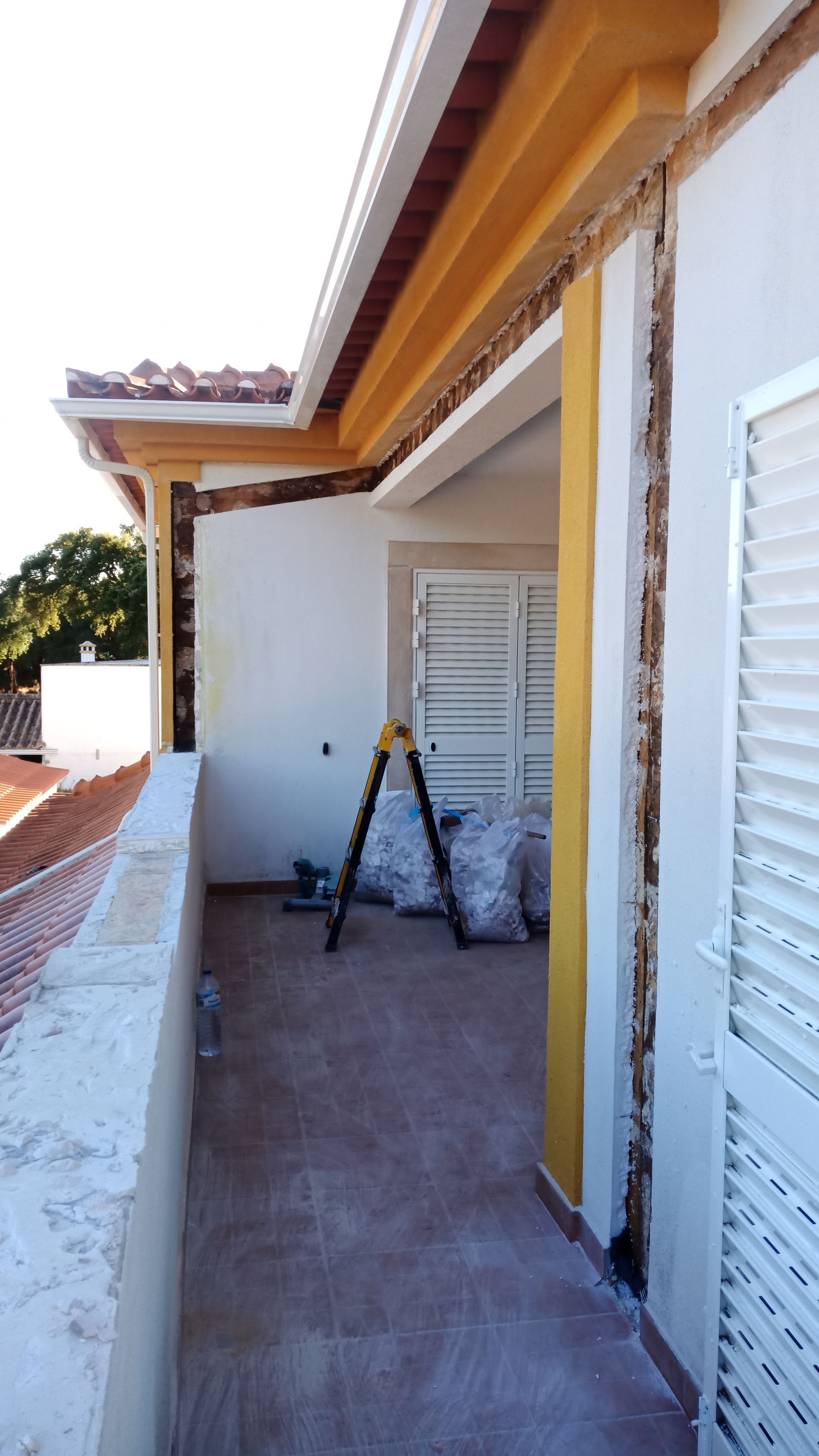 Reforma de varanda com escada, bolsas e estrutura de parede exposta. Detalhes em amarelo e branco.