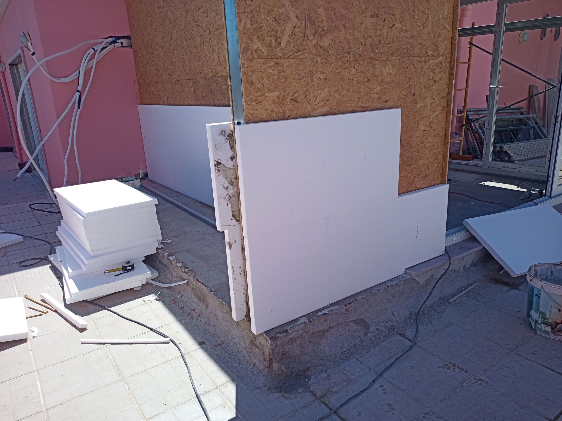 Canteiro de obras com painéis de isopor sendo instalados em uma parede.