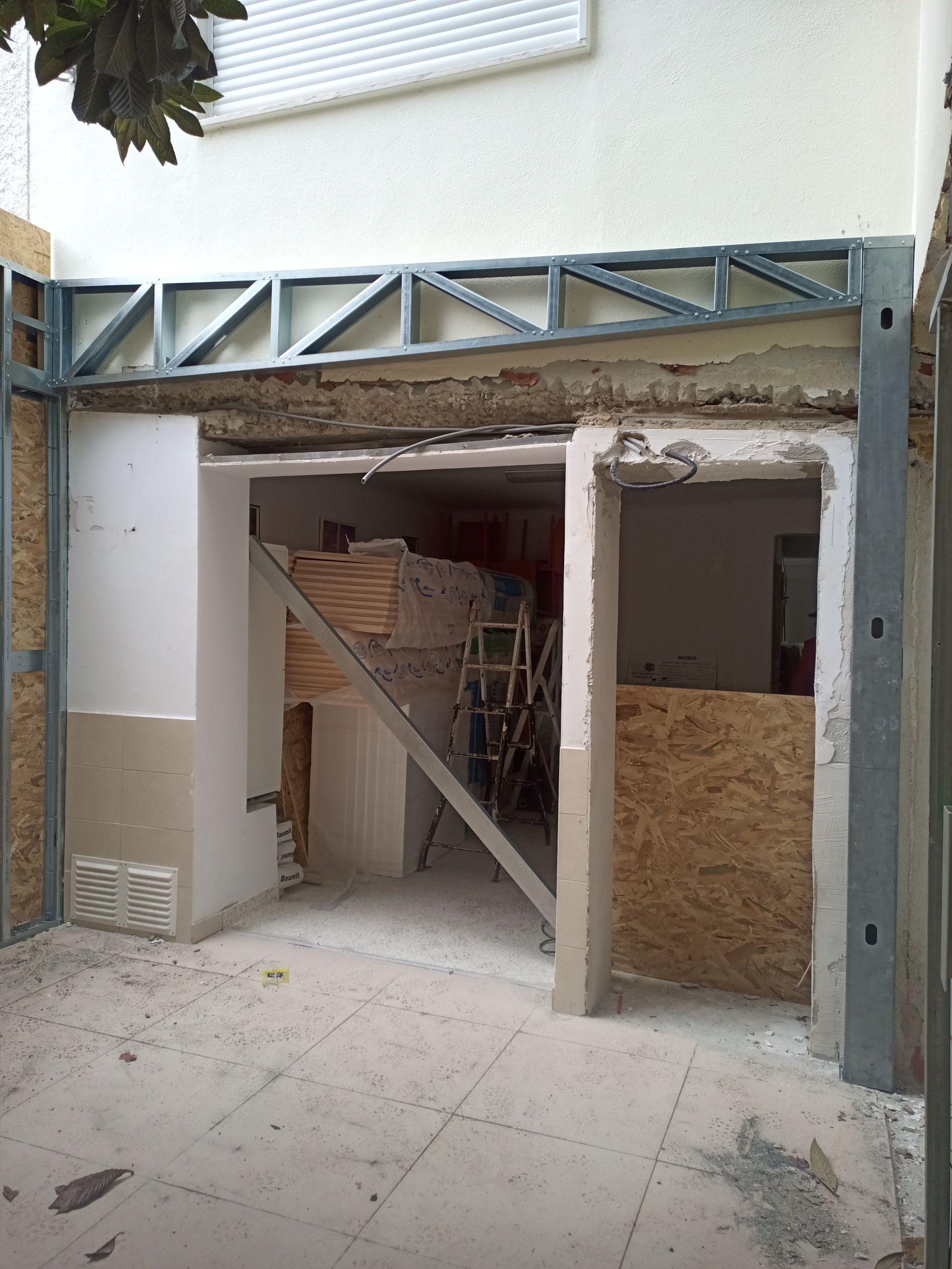 Canteiro de obras: porta com estrutura metálica, suportes temporários no interior, paredes inacabadas, ambiente externo.