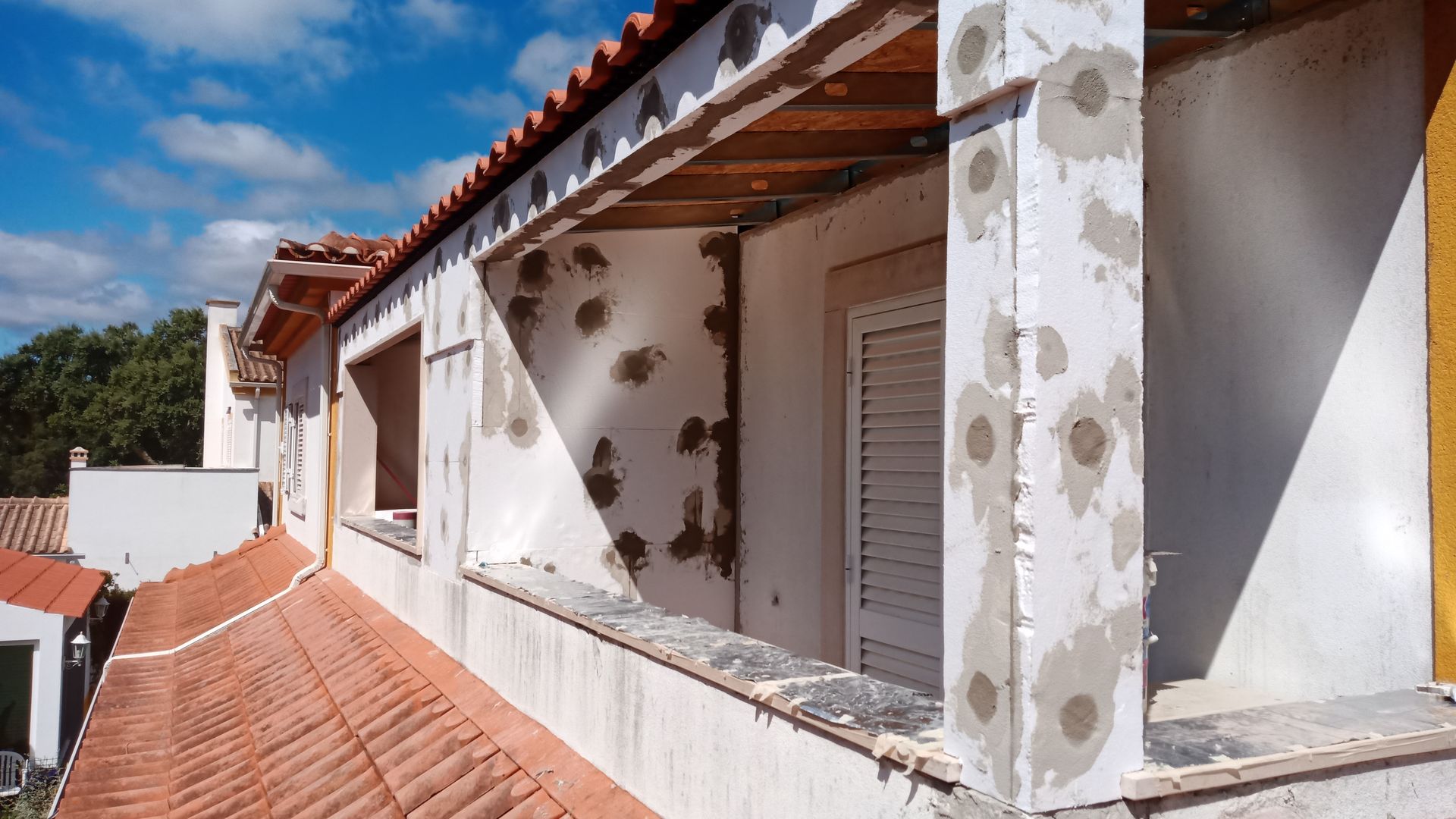 Exterior do prédio em construção; paredes brancas, telhado marrom, céu azul.