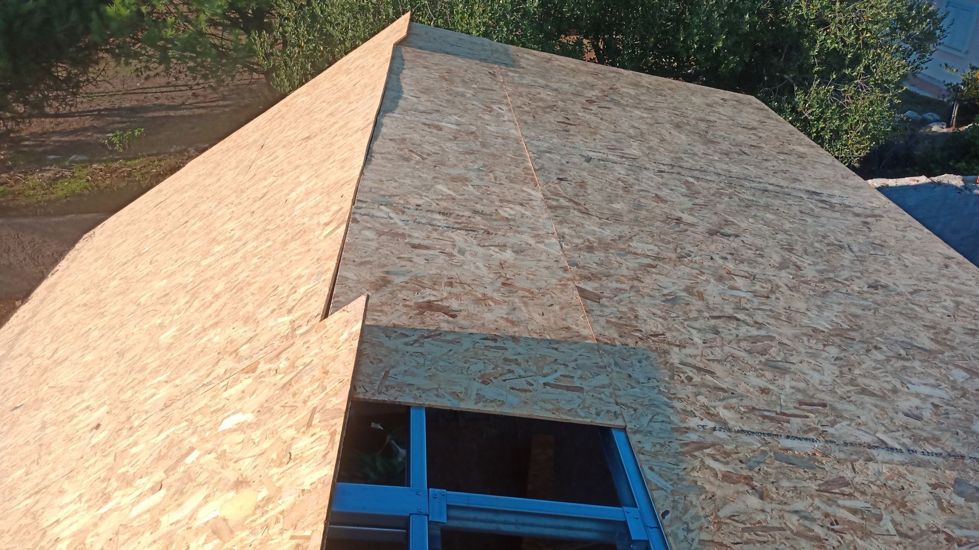 Revestimento de OSB no telhado; uma moldura de janela azul é visível.