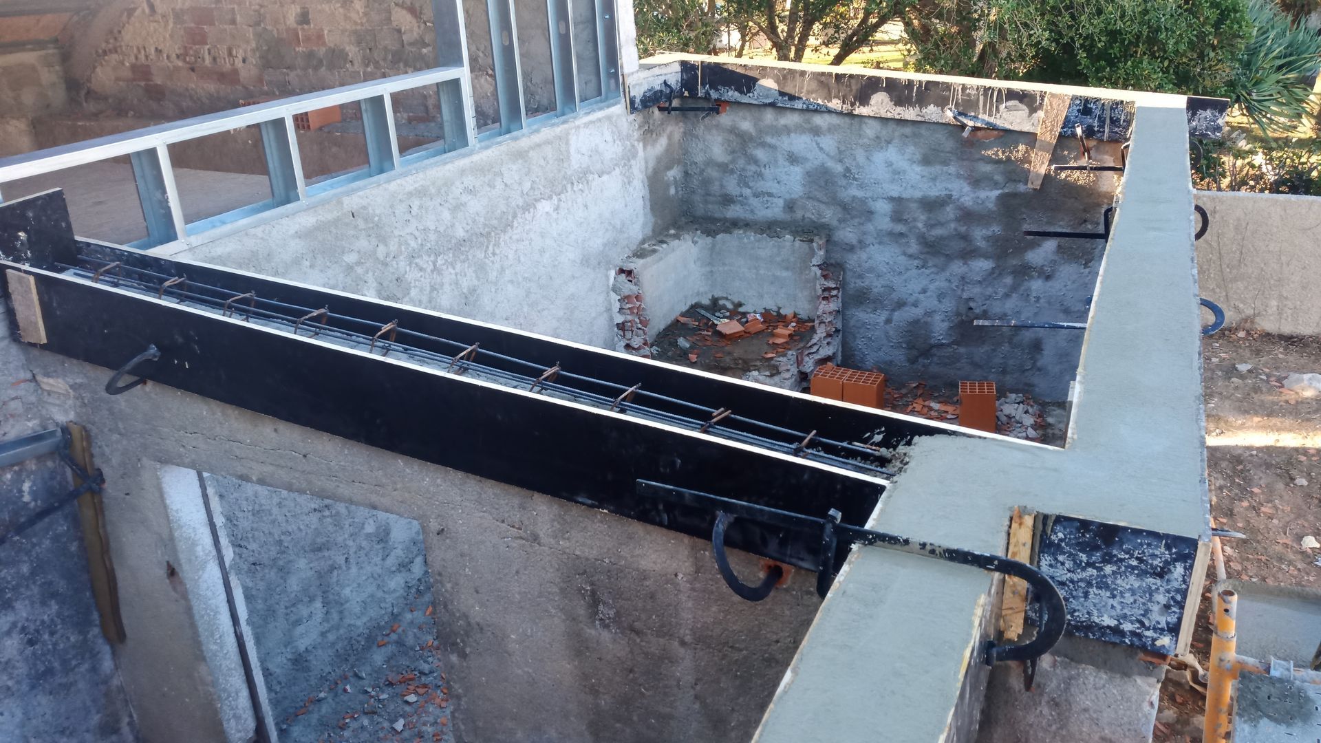 Construção de uma churrasqueira externa de concreto com vigas de suporte de metal e uma abertura retangular.