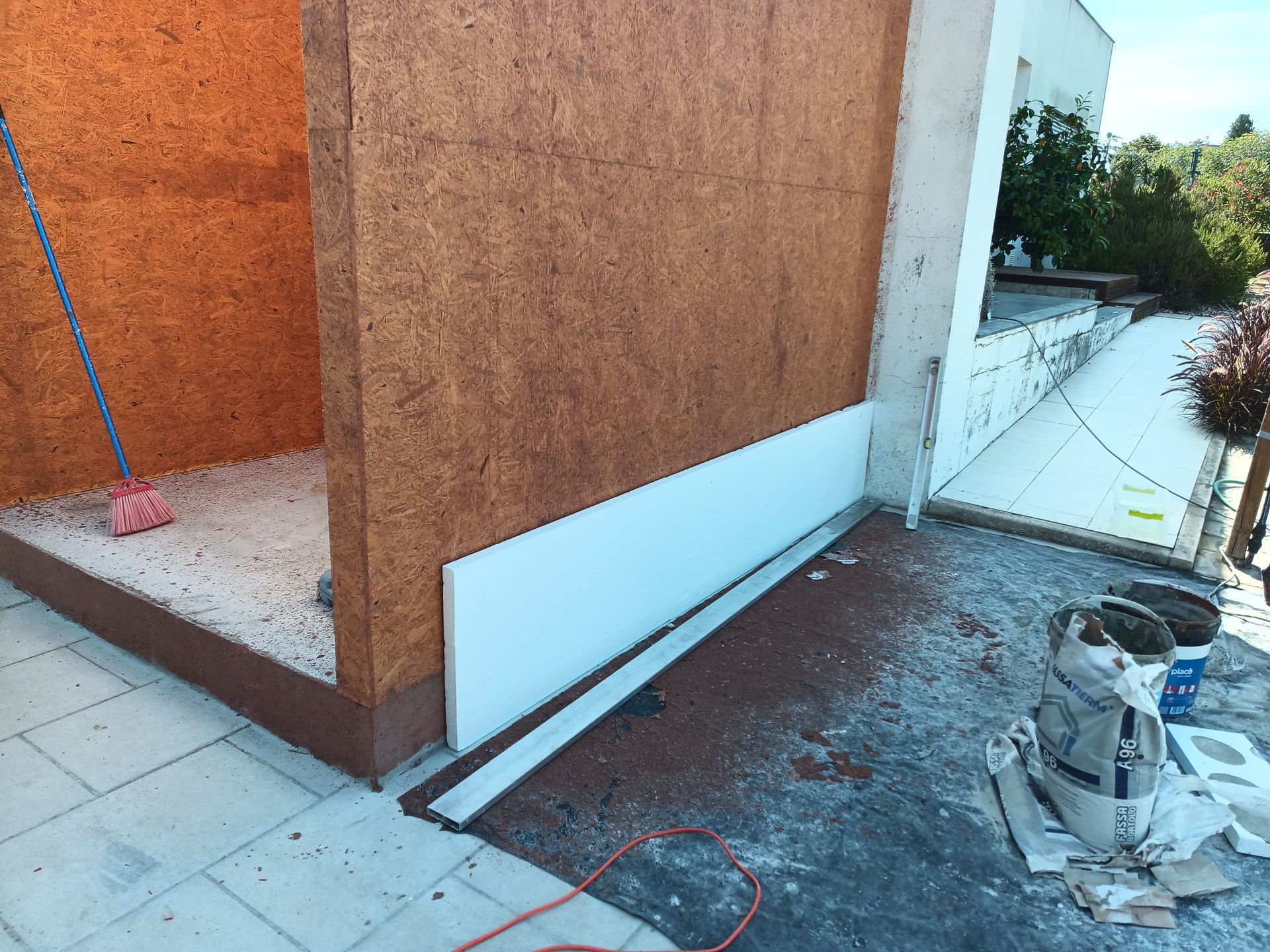 Canteiro de obras: Parede com placa isolante branca instalada. Painéis OSB visíveis. Ambiente externo.