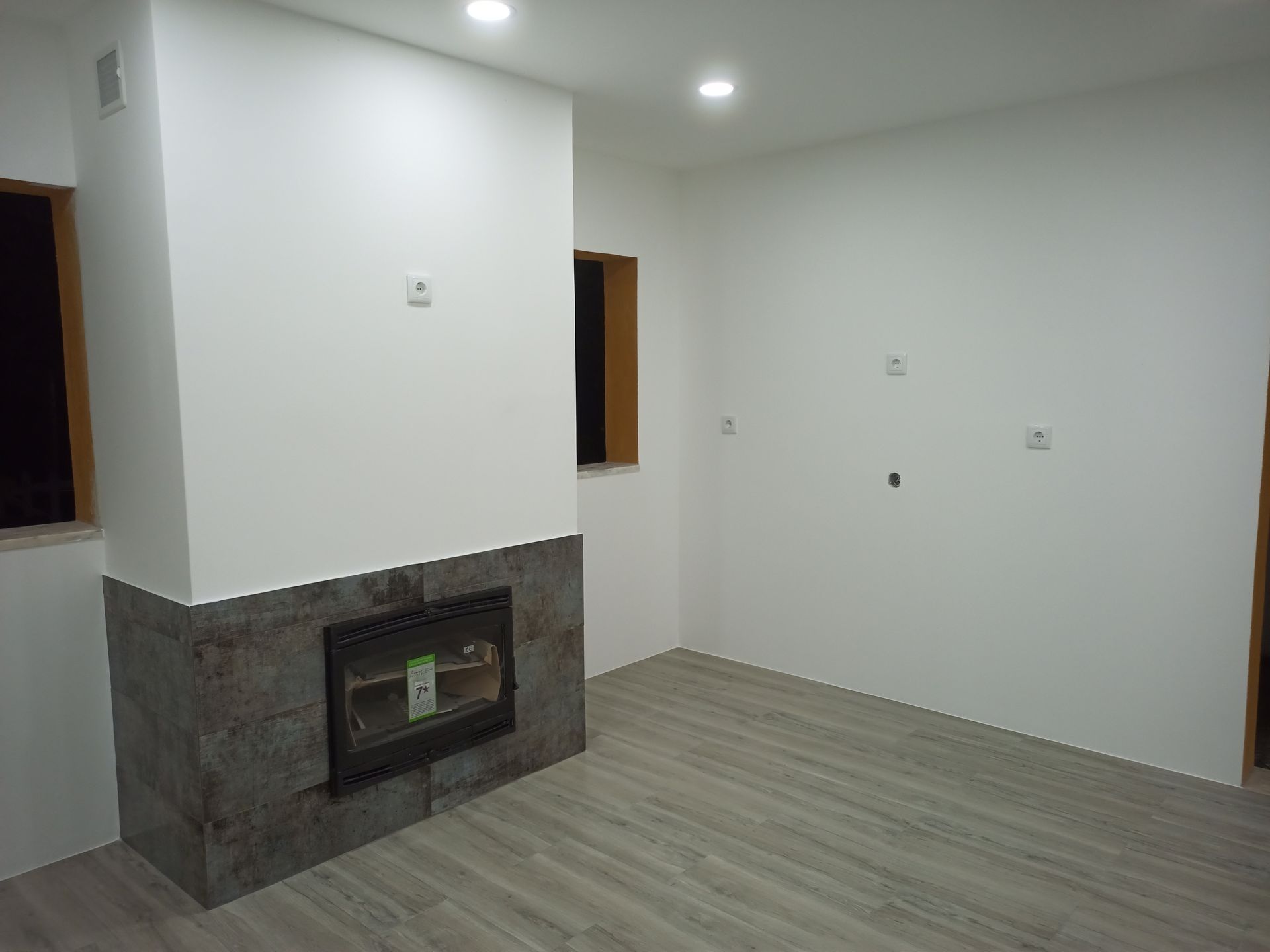 Um quarto vazio com lareira, piso cinza claro e paredes brancas.
