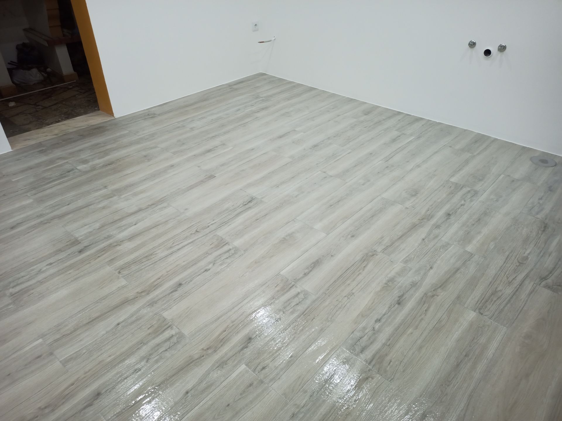Piso de cerâmica imitando madeira em tom claro em um canto da sala; paredes brancas.