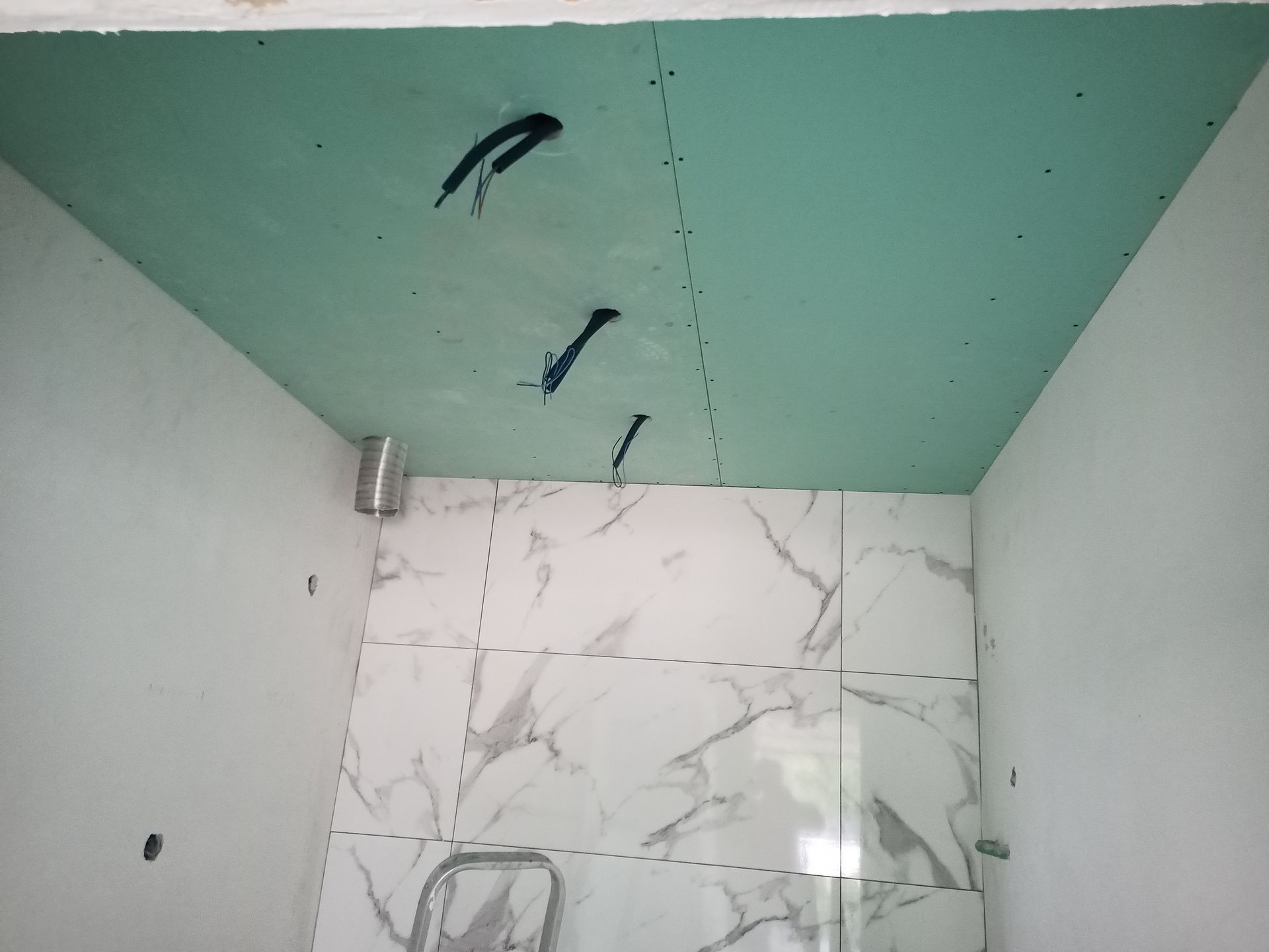 Banheiro em construção com teto de gesso verde, paredes brancas e azulejos com estampa de mármore.