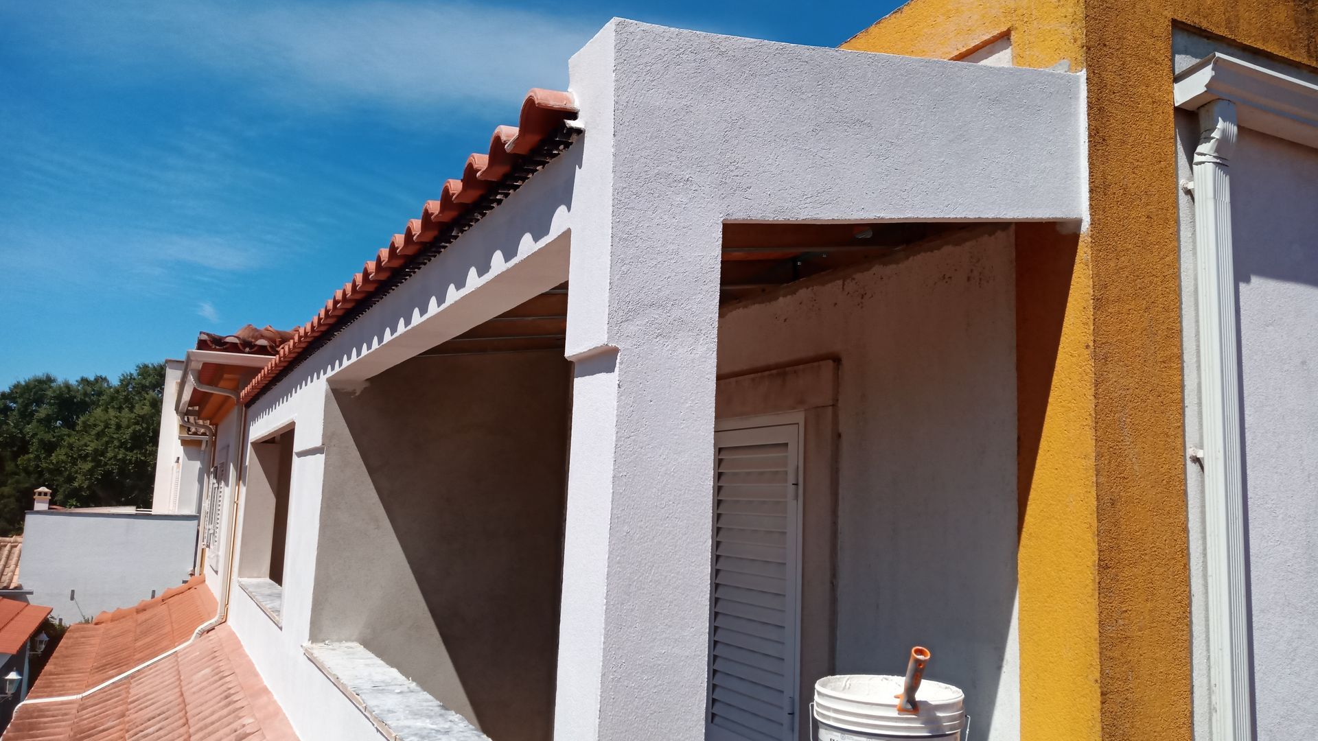 Exterior do edifício com fachada de estuque branco e telhado de telha laranja contra um céu azul.