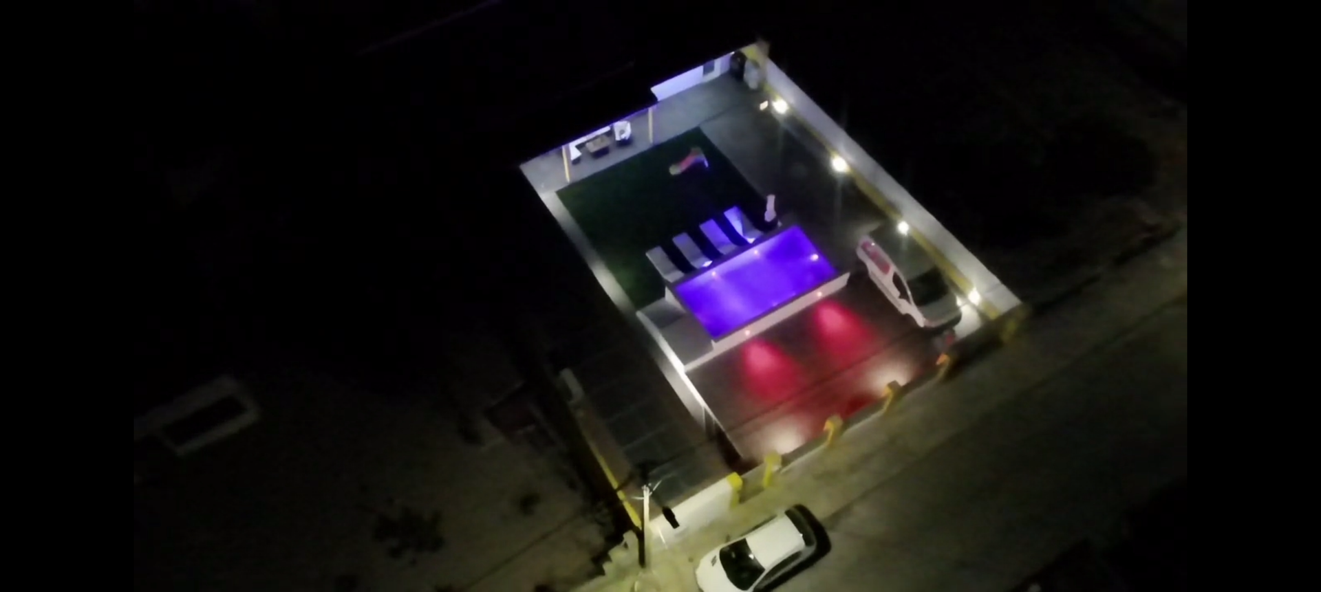 Vista aérea de uma área de piscina bem iluminada à noite. Carros são visíveis na periferia. A piscina está iluminada em tons de roxo e vermelho.