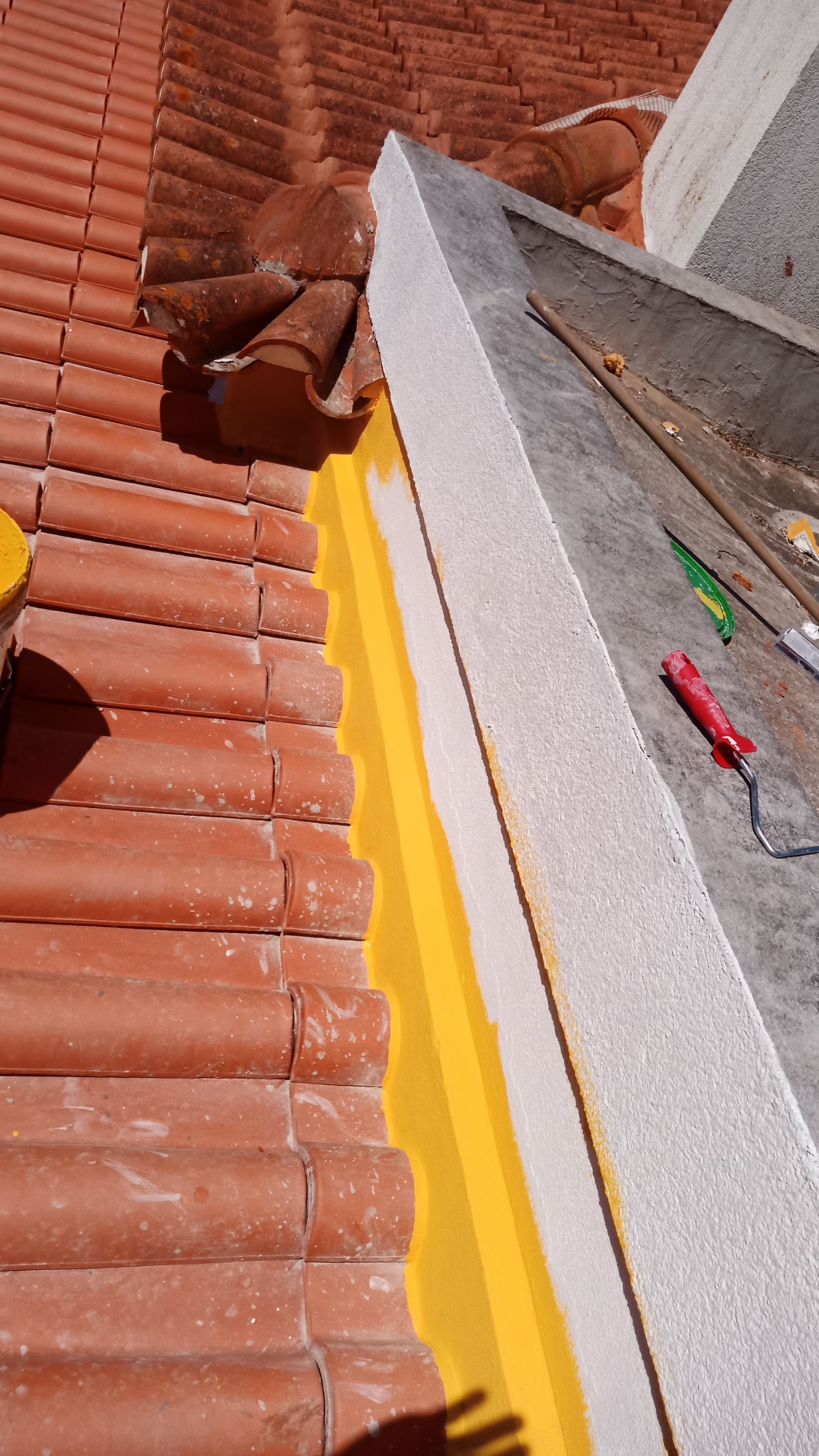 Reparo de telhado: beiral de telha vermelha com selante amarelo e acabamento branco junto a uma parede de concreto.