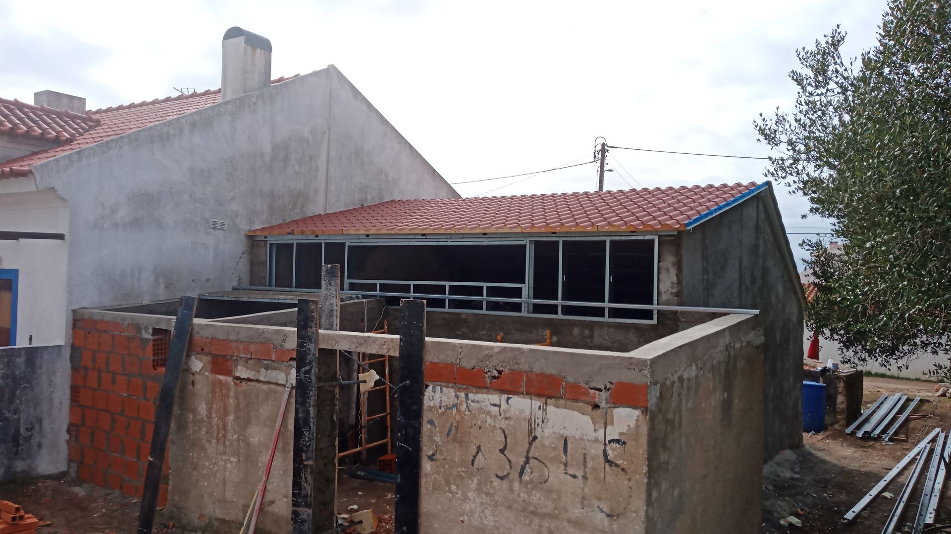 Prédio em construção, com telhado de telha e alvenaria aparente. Estrutura adjacente com fechamento envidraçado.
